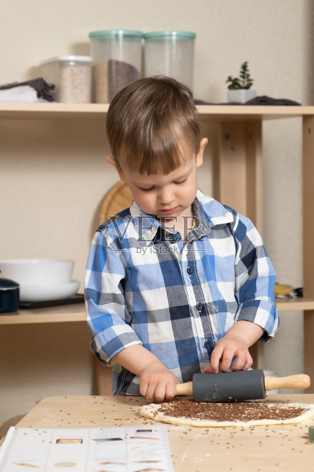 孩子用擀面杖擀面，做了他的第一块饼干。孩子们在厨房里。照片摄影图片