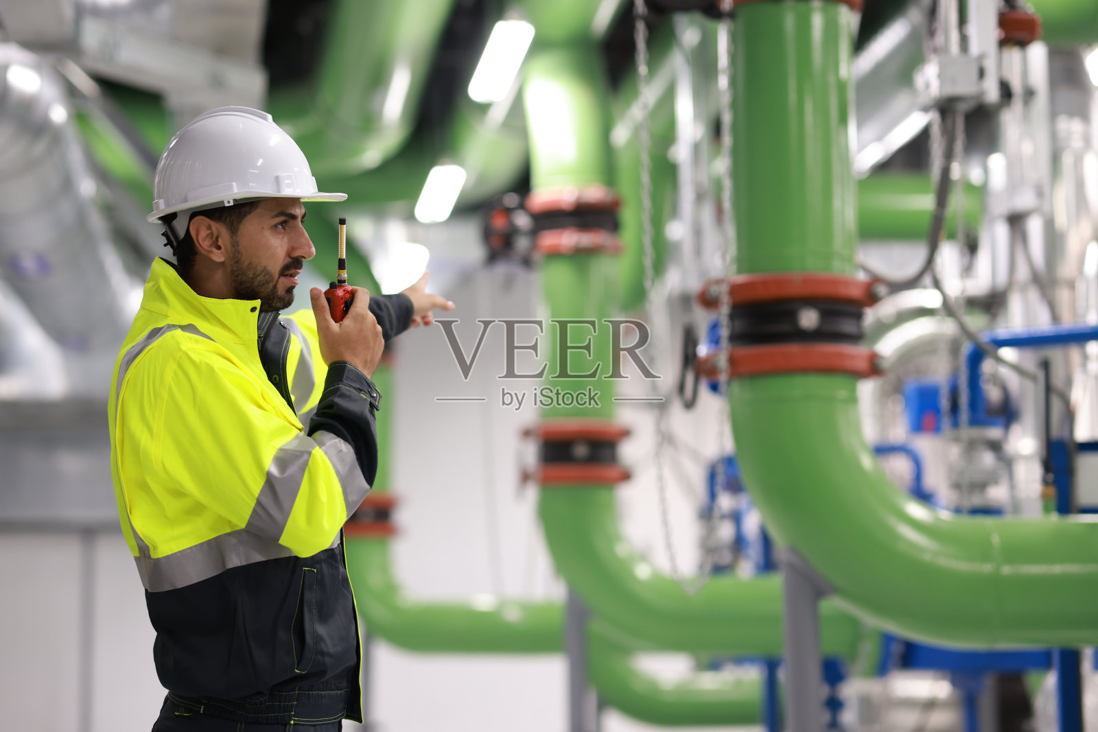 英俊的暖通空调系统工程师的肖像，穿着绿色安全夹克和头盔在机器上工作照片摄影图片