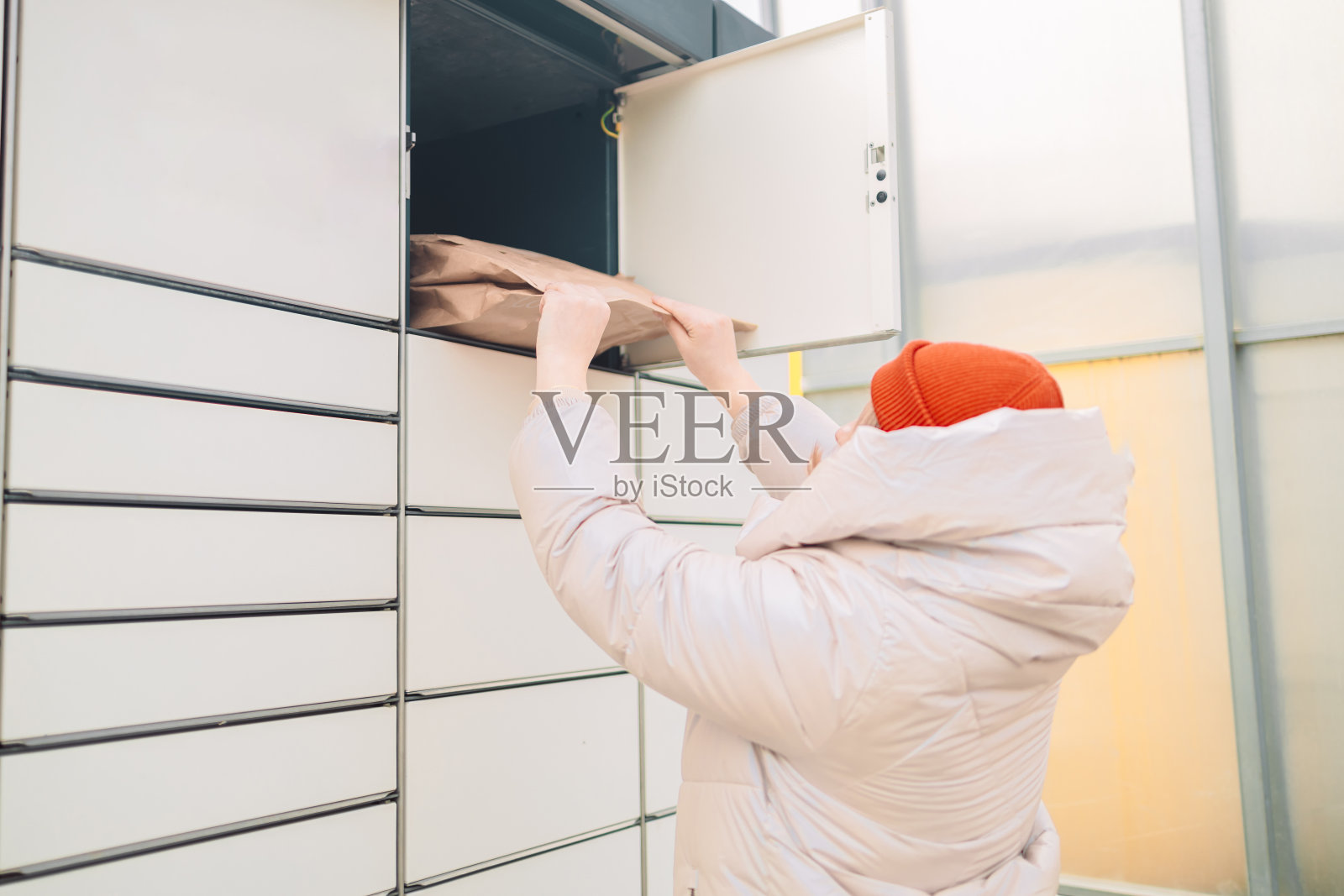 在户外自动包裹机前拿着盒子的妇女。户外有许多邮筒的现代包裹寄存柜照片摄影图片