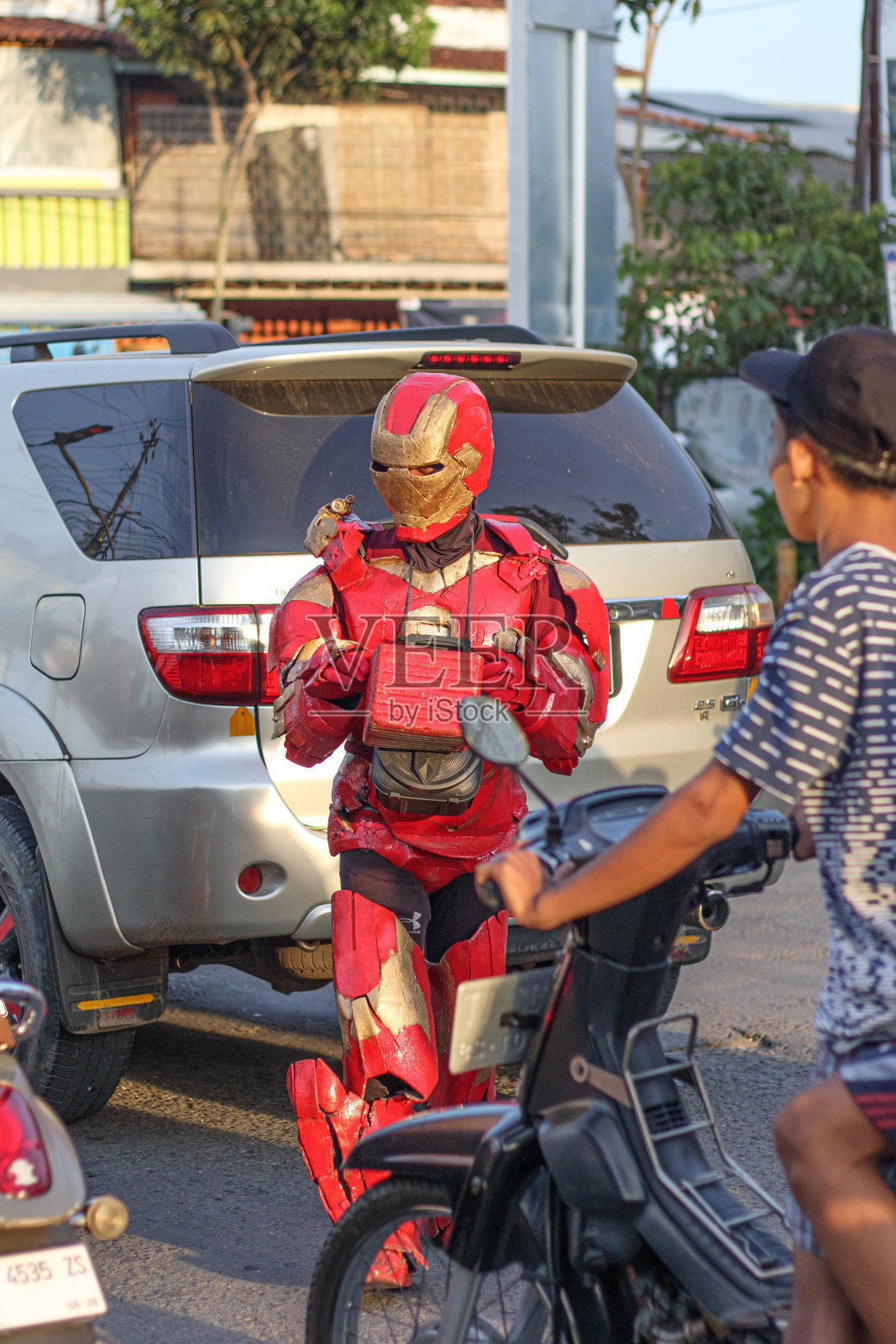 一个穿着钢铁侠英雄服装的年轻人站在一个满是摩托车的红绿灯前照片摄影图片