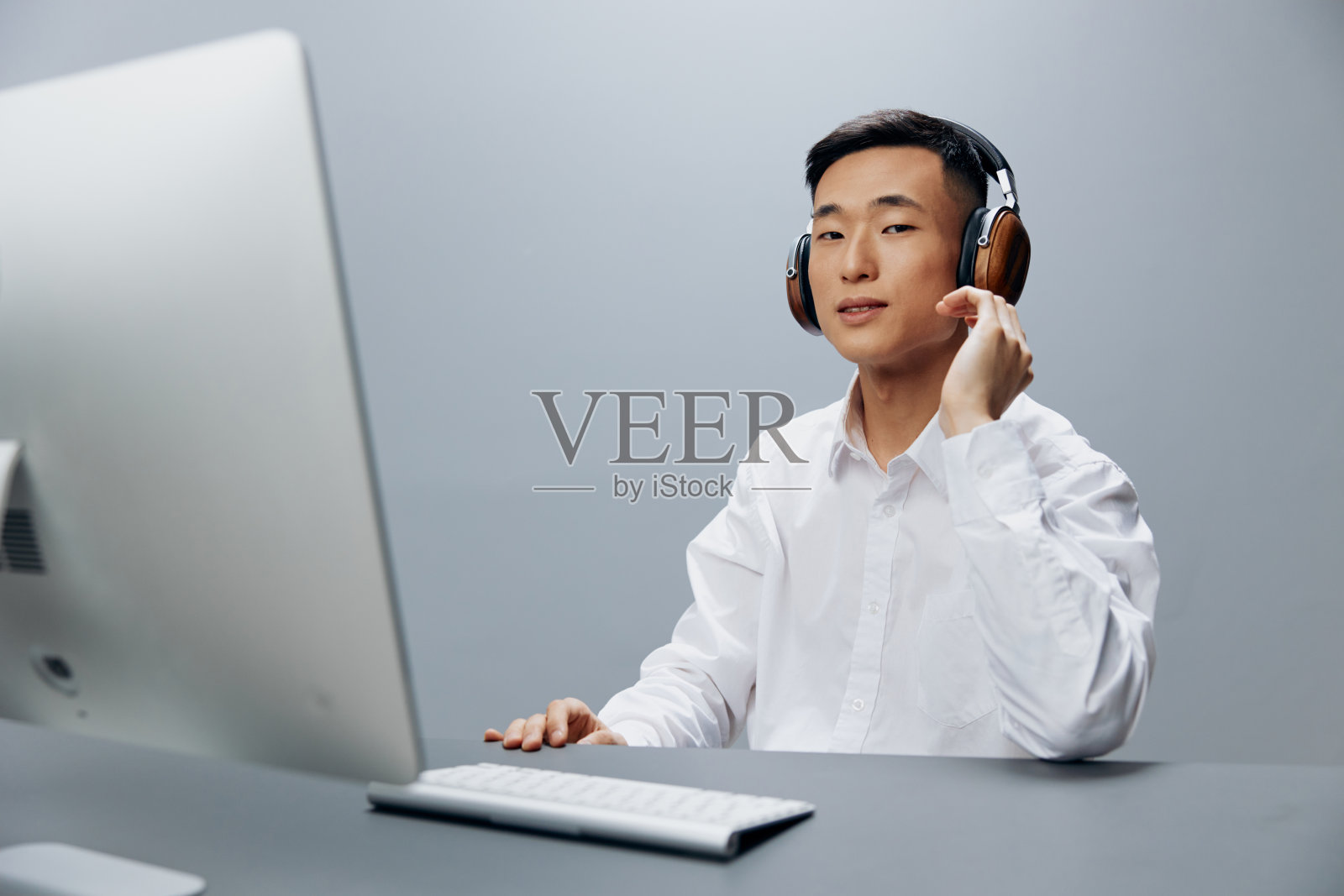 一个穿着白衬衫戴着耳机的亚洲人坐在办公室里工作照片摄影图片