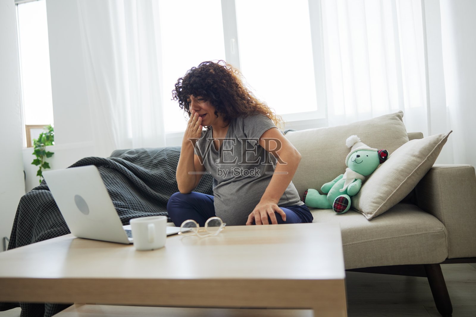 一位孕妇微笑着坐在家里的沙发上，用笔记本电脑看电视节目、电影和连续剧。孕妇的生活方式，准备分娩，怀孕的最后一个月照片摄影图片