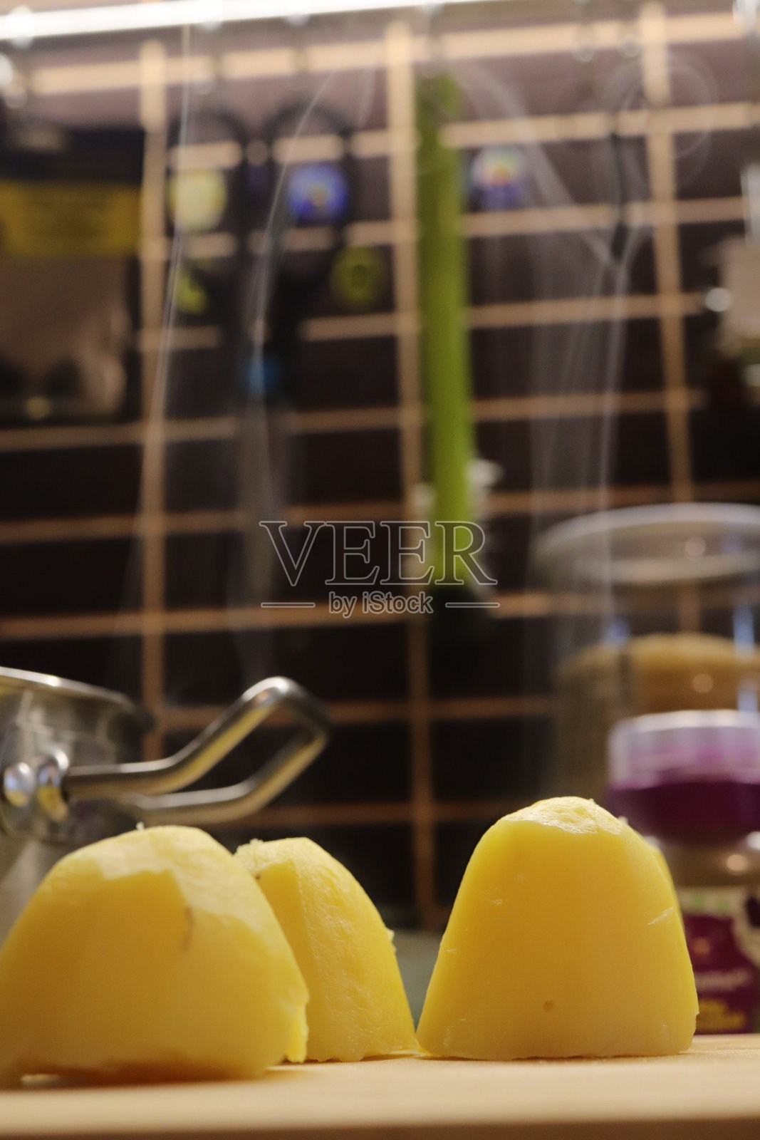 刚煮好的冒着热气的土豆躺在砧板上，厨房是背景。照片摄影图片