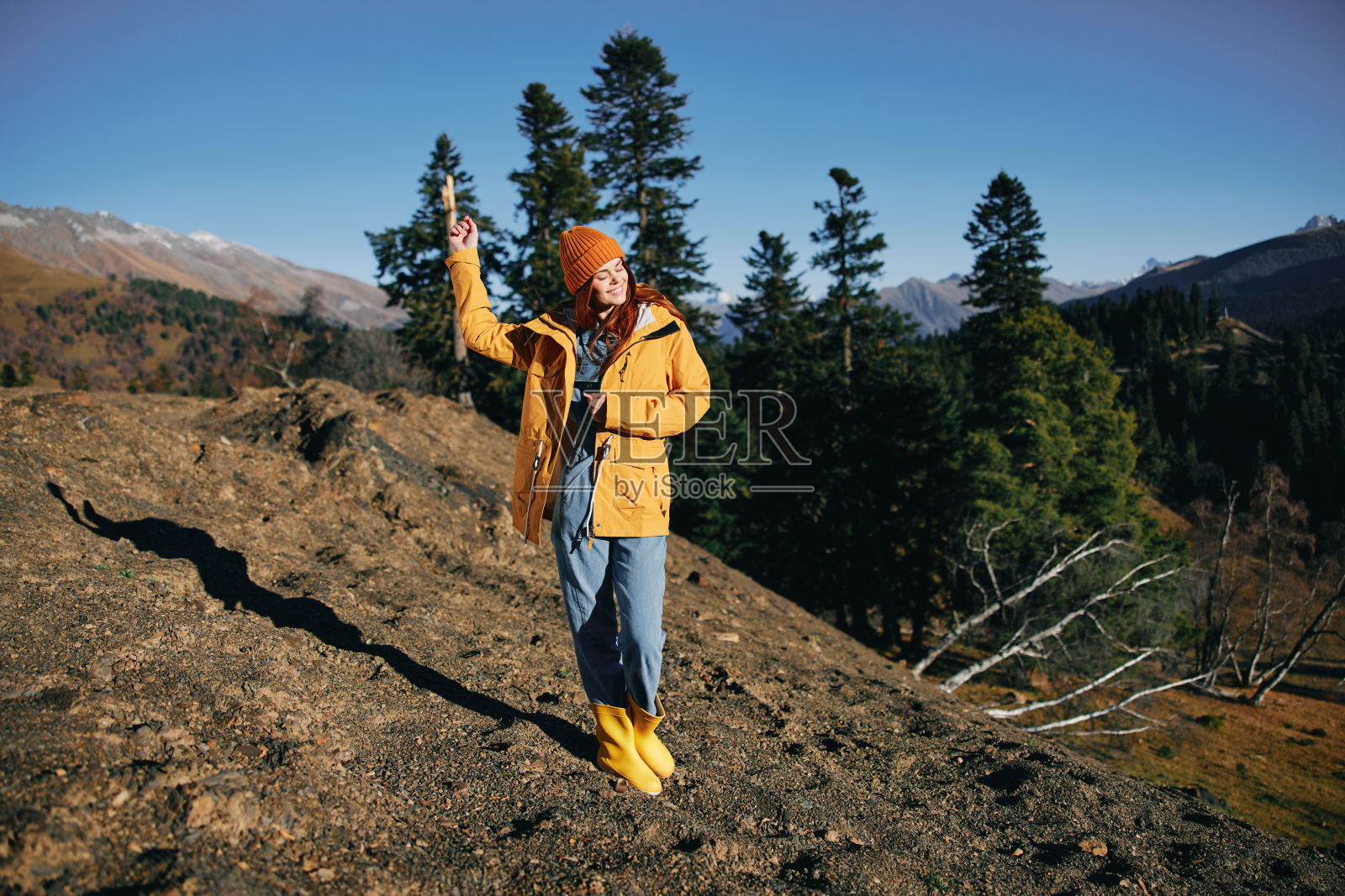 女人在山间徒步行走，看着大自然秋色的景色，披着黄色的披肩，戴着长长的幸福帽子照片摄影图片