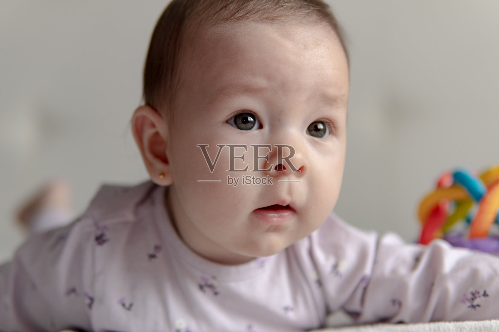 一个6个月大的女婴躺在白色的床上玩她的玩具。照片摄影图片