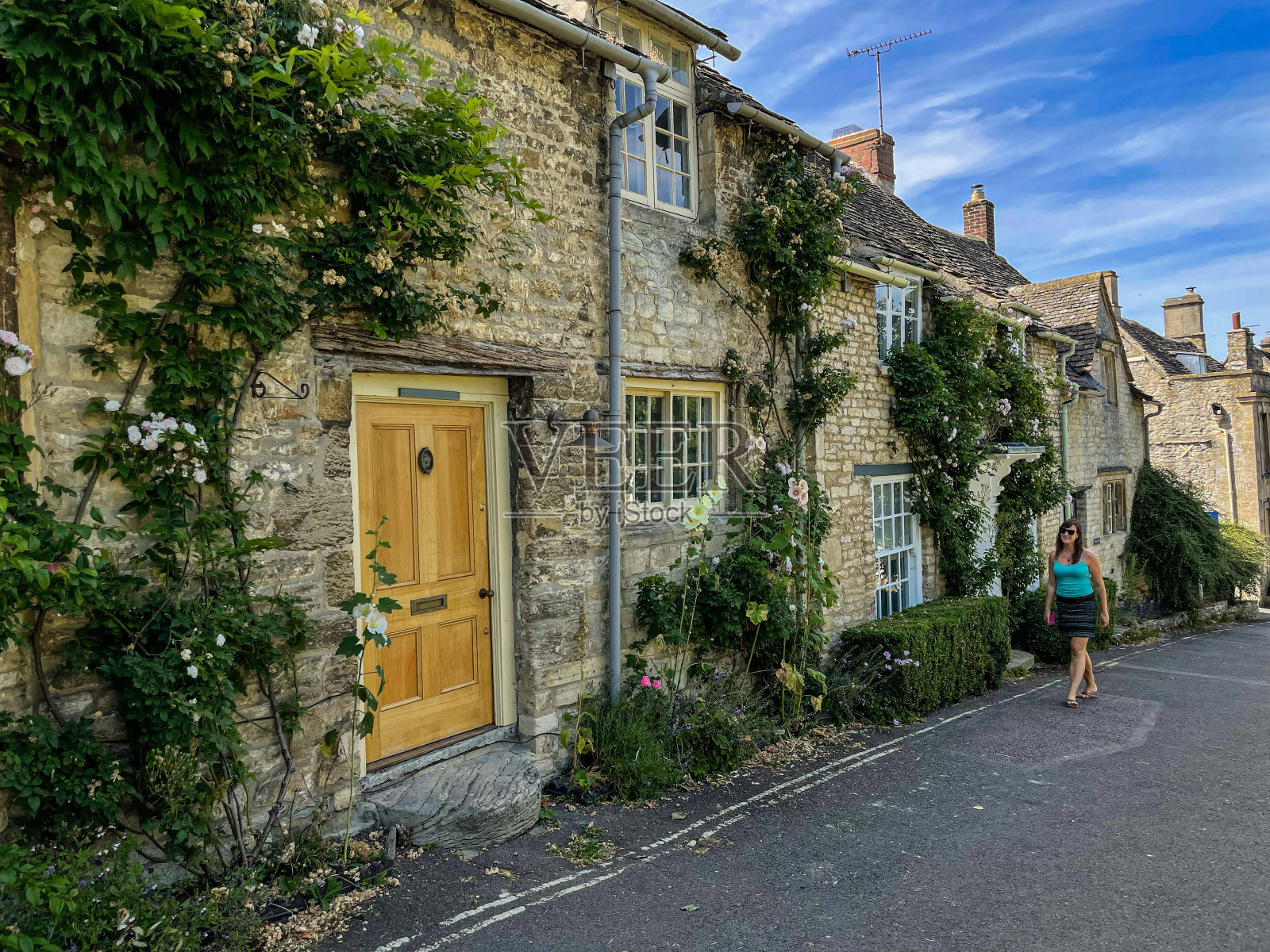 微笑的女人走在铺满鲜花的石屋的迷人街道上照片摄影图片