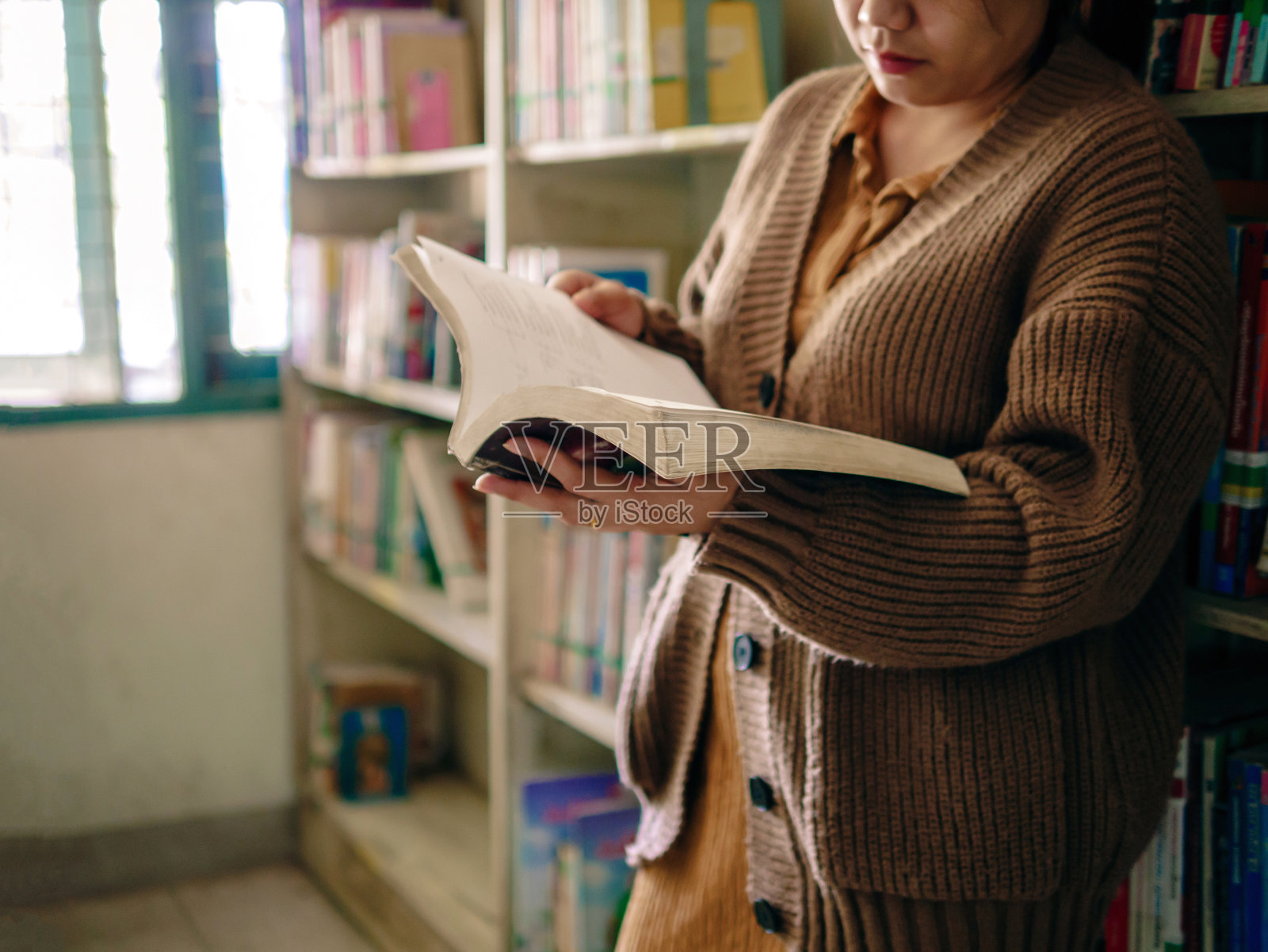 学习，教育老年妇女手捧一本书站在图书馆的窗口，在早晨，放松和享受书籍。照片摄影图片