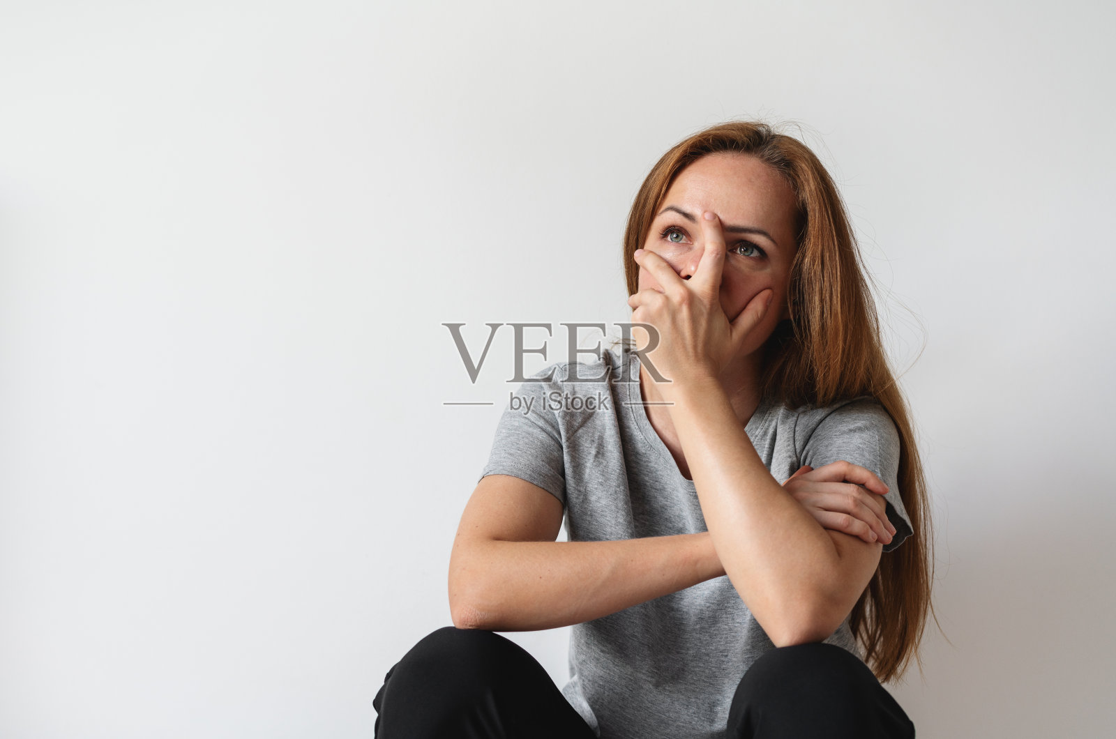 不快乐的沮丧女子坐在灰色的墙边，用手捂着脸，创伤后应激障碍照片摄影图片