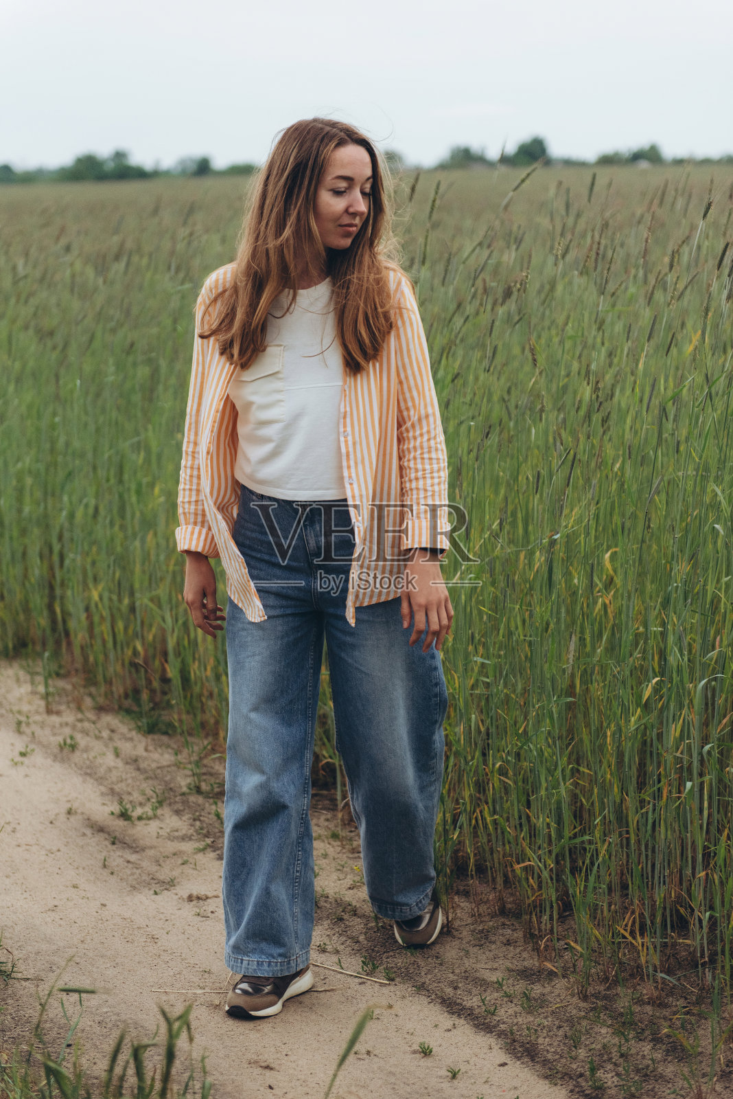 一个女孩，一个女人，站在绿色麦田中间的路上。照片摄影图片
