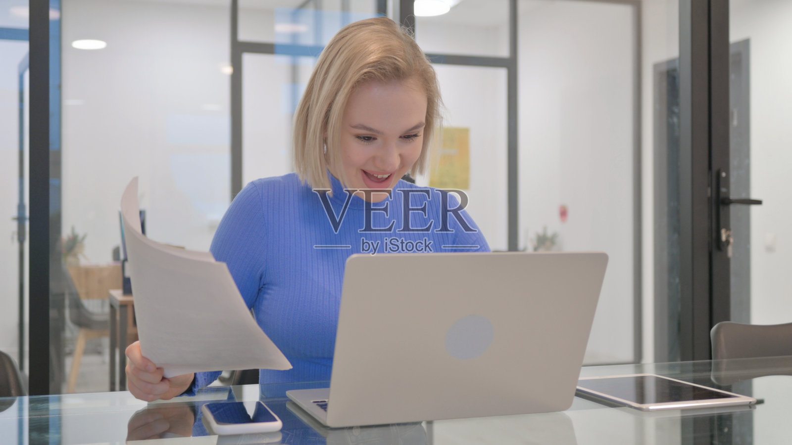 年轻女子一边使用笔记本电脑和文件一边庆祝照片摄影图片