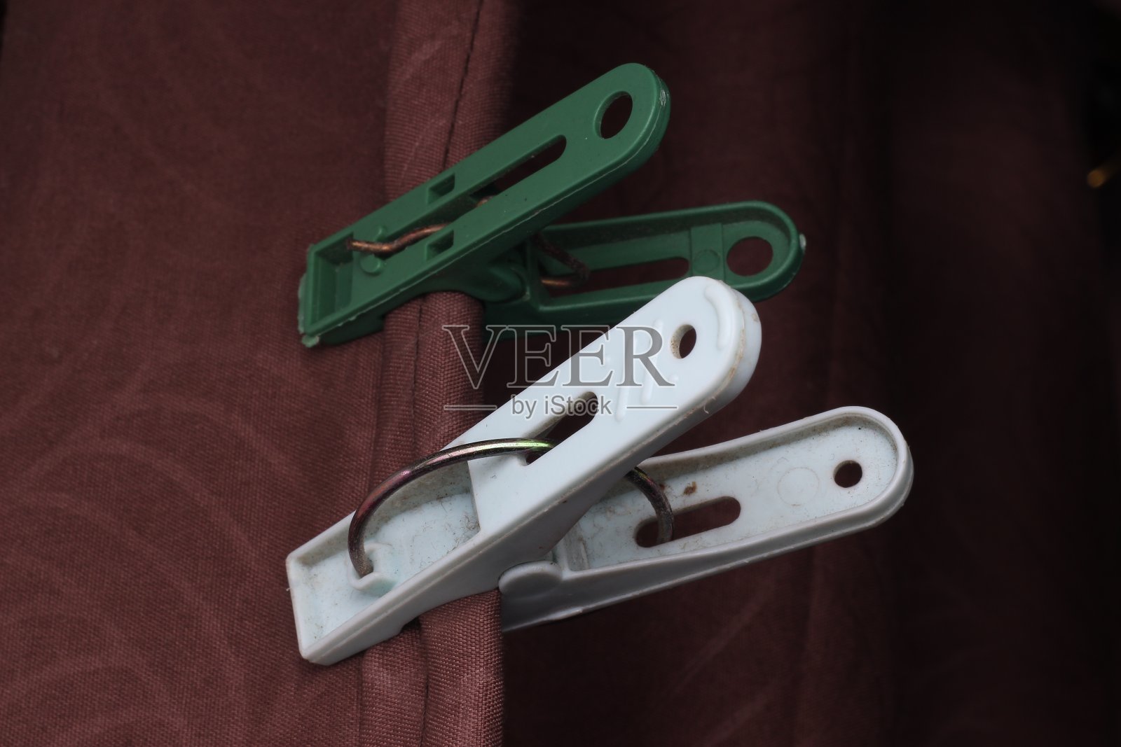 两个白色和绿色的衣服别针系在深黑色背景上的栗色布料上照片摄影图片