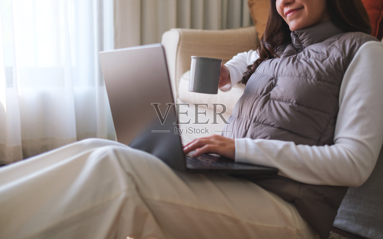 一个年轻女子在家里边喝咖啡边用笔记本电脑工作的特写照片摄影图片