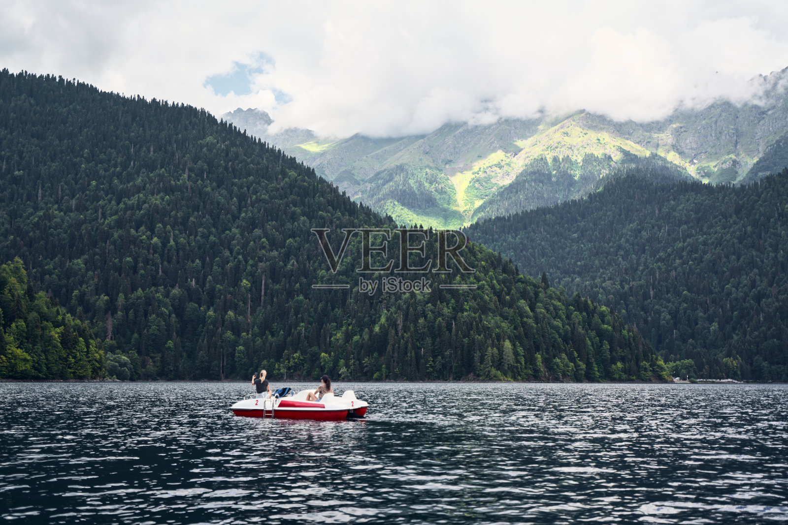 在群山环绕的湖中央，一位年轻女子坐在划桨船上照片摄影图片