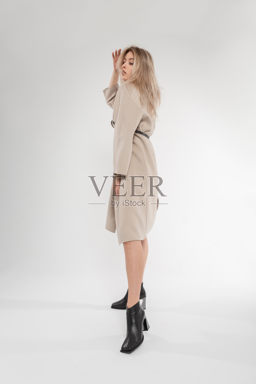漂亮性感的年轻女模特穿着时尚经典的米色外套和黑色皮鞋，在白色背景的工作室里摆姿势。时尚的新春季系列外衣照片摄影图片