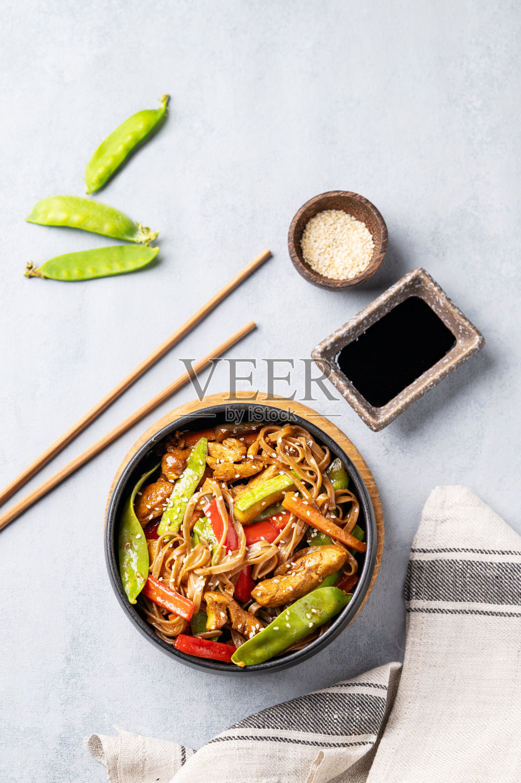 用筷子、酱油和芝麻在浅色背景下与荞麦面、肉和蔬菜一起翻炒。照片摄影图片