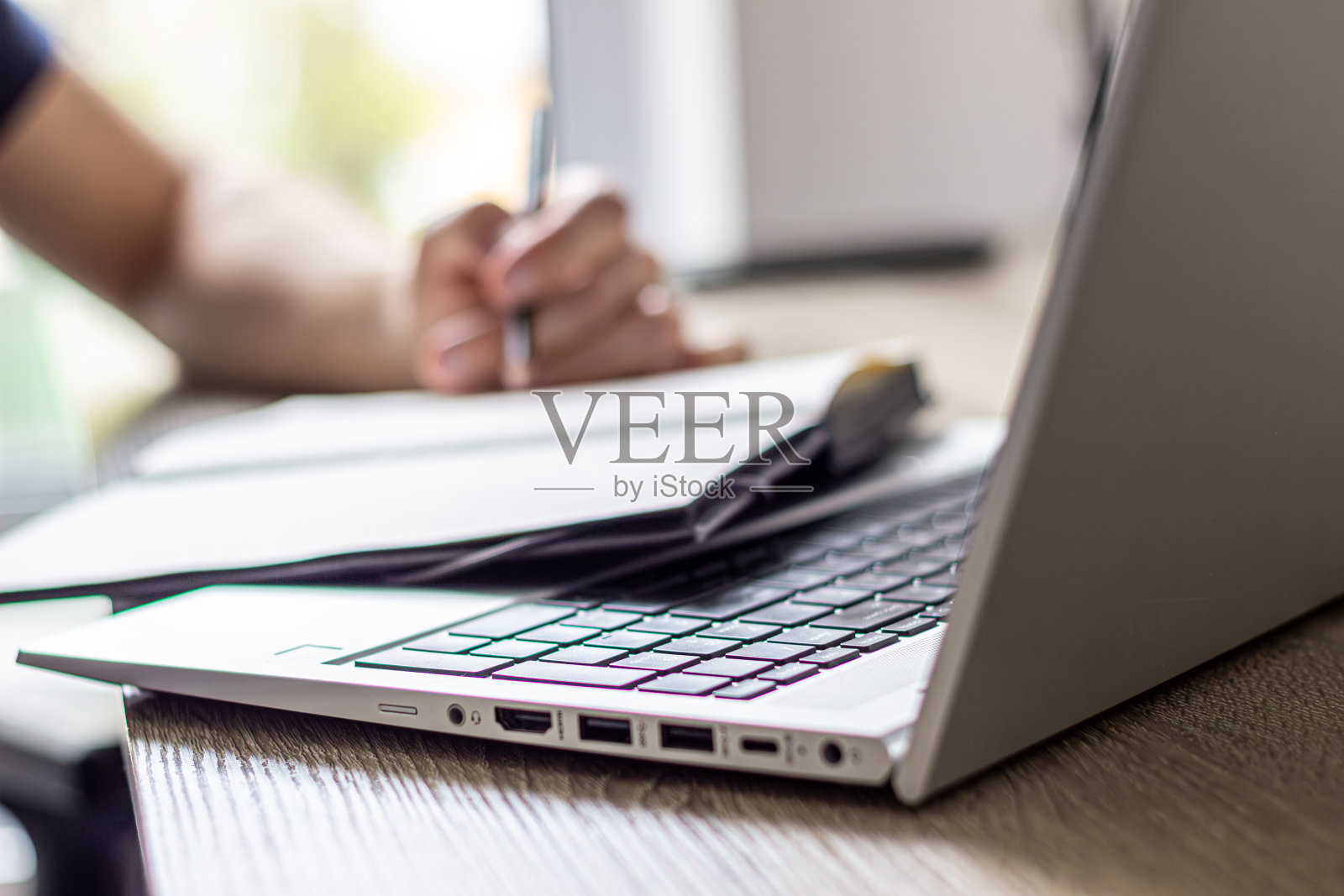 笔记本电脑在焦点上，男人在背景上在纸笔记本上做笔记，家庭办公室照片摄影图片