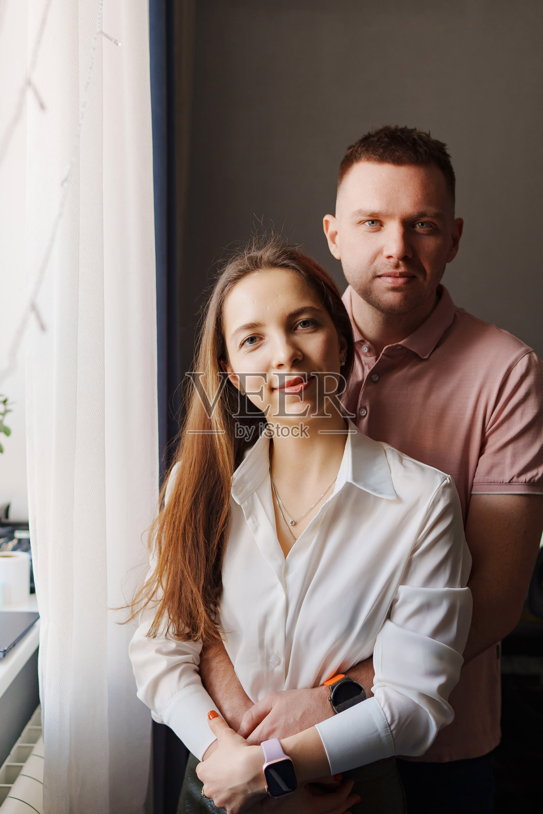 幸福的已婚夫妇在公寓的窗户前拥抱。照片摄影图片