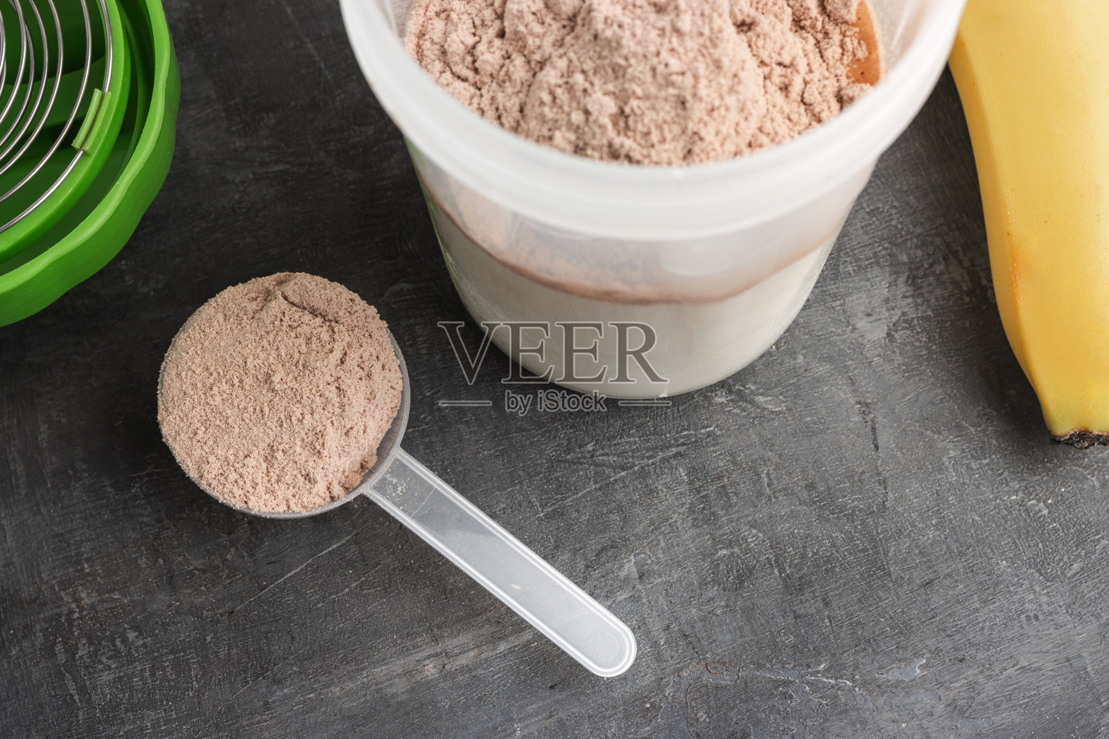 乳清蛋白粉中加入巧克力味的塑料量勺，摇壶中加入牛奶和香蕉，深色背景，制作蛋白摇饮的过程照片摄影图片