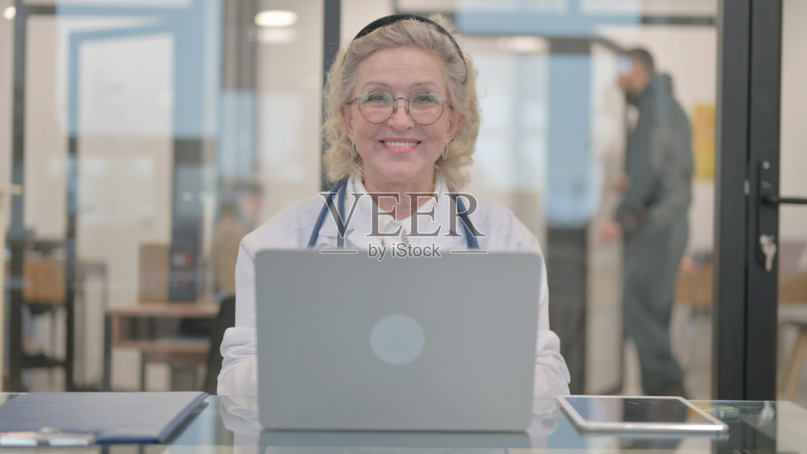 资深女医生一边摆弄笔记本电脑，一边对着镜头微笑照片摄影图片