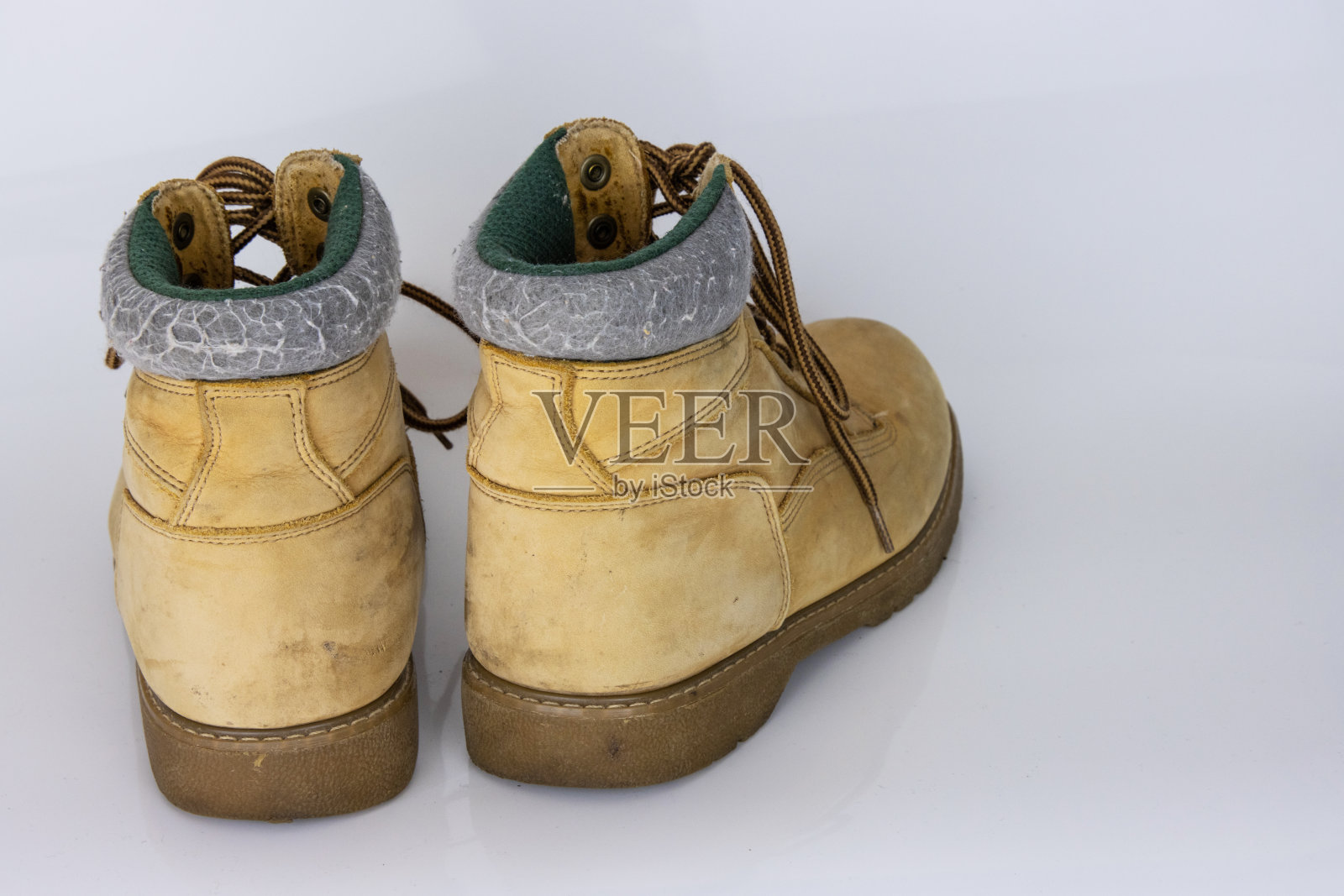 一双旧的黄色徒步旅行蕾丝靴，隔离在白色光滑的表面上，具有美丽的反射效果。二手旅游步行鞋。后视图。副本的空间。白色背景。照片摄影图片