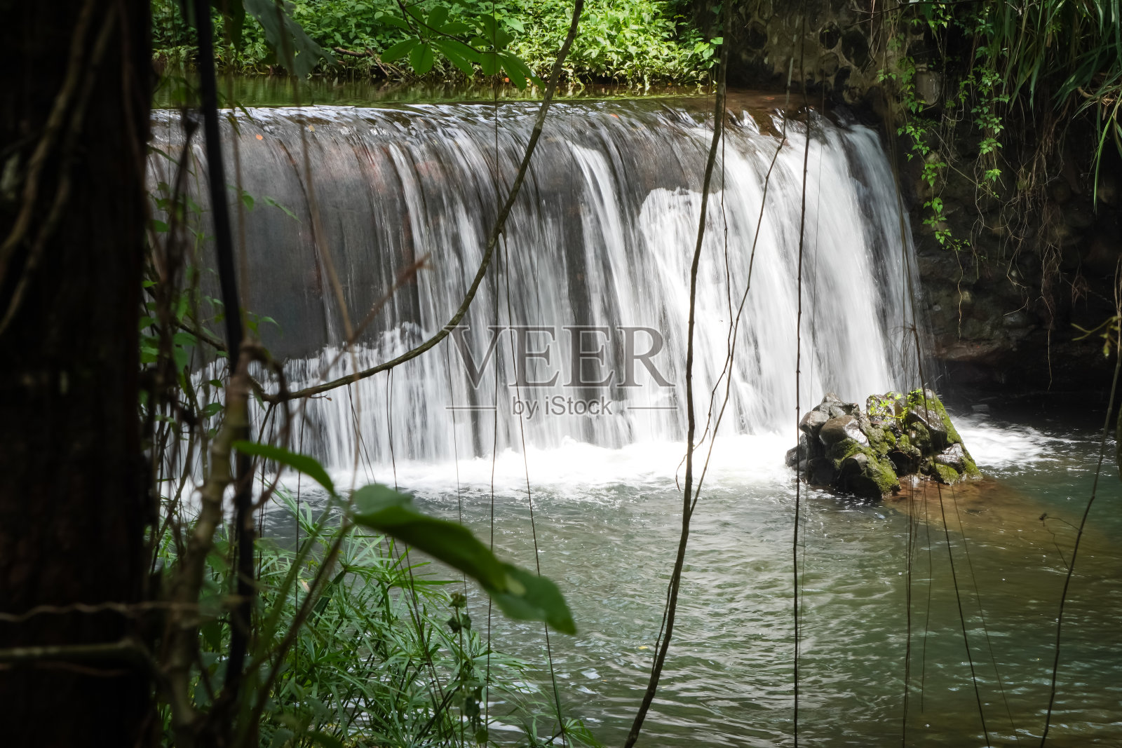 长曝光摄影-大坝在岩石河与清澈的水自然池周围的树木和藤蔓。印度尼西亚日惹Sleman的人工瀑布。环境概念照片摄影图片