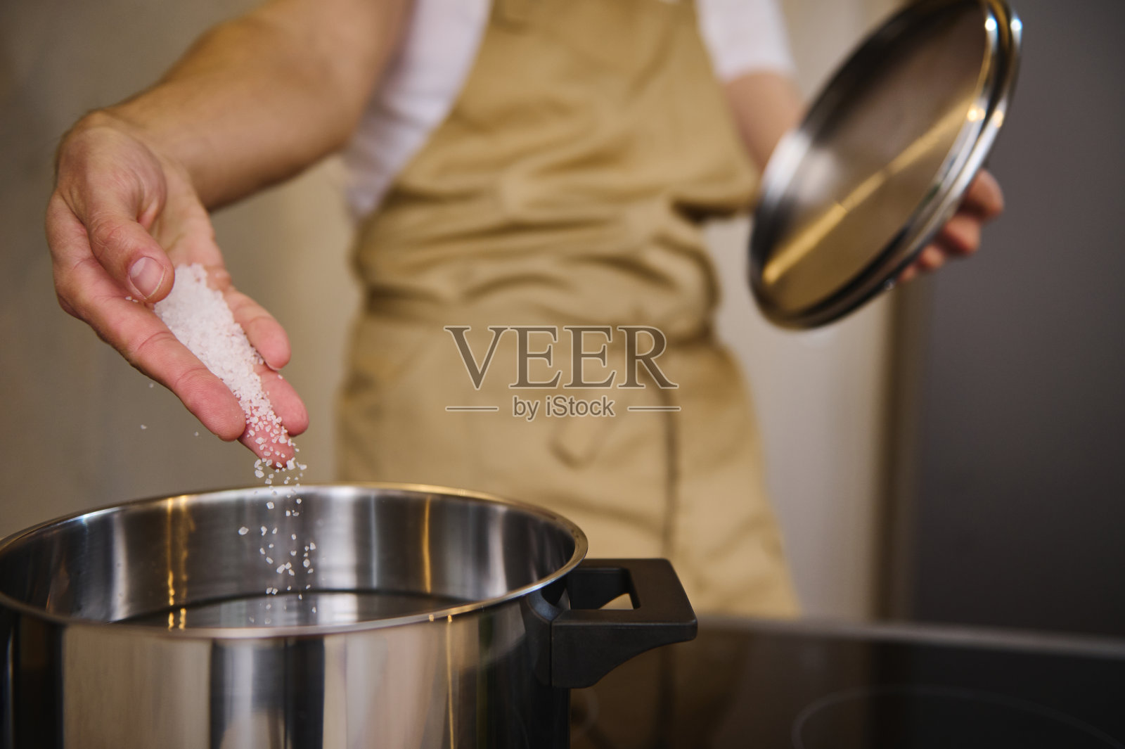 厨师站在电炉前，往不锈钢炖锅里的沸水里加盐，煮意大利面或其他食物的特写照片摄影图片