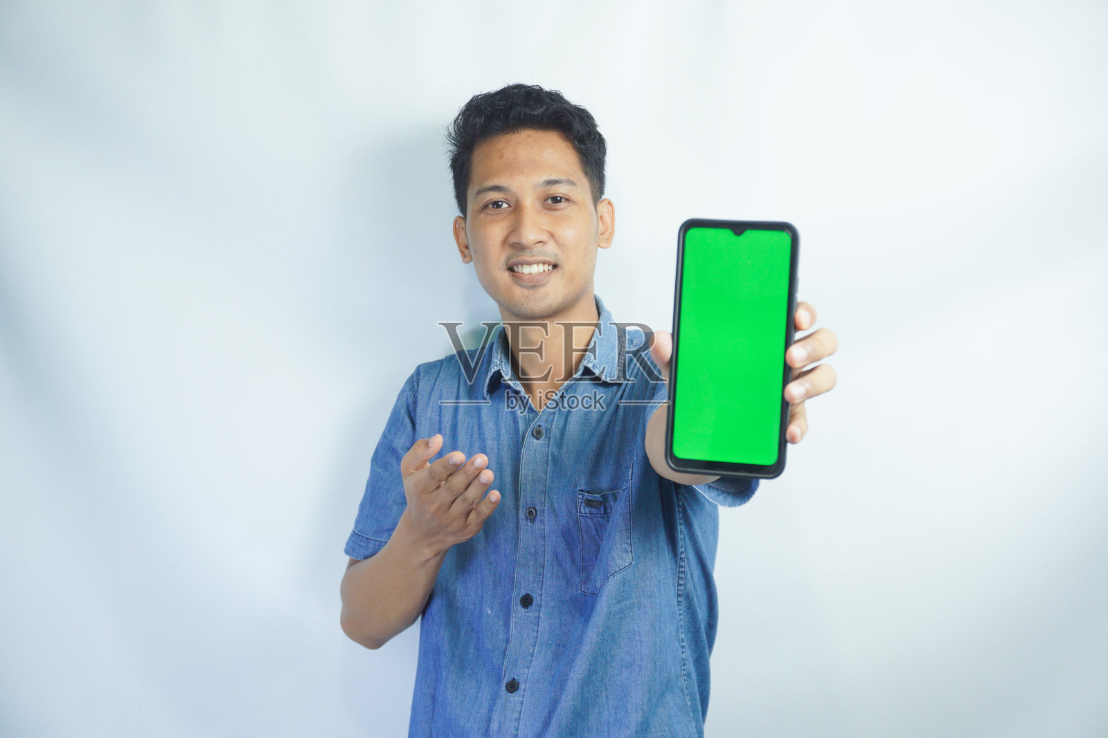 一名亚洲男子的画像，手里拿着一个绿色的大屏幕智能手机，展示并指着这个设备，横幅照片摄影图片