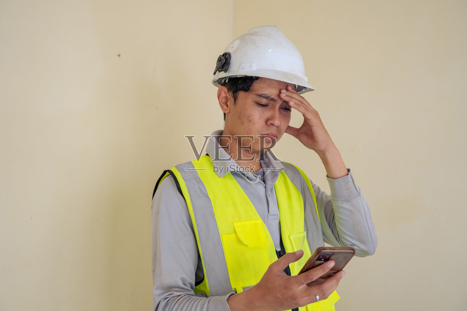 年轻的建筑工人戴着可穿戴包，拿起电话，摆出惊讶的姿势。照片摄影图片