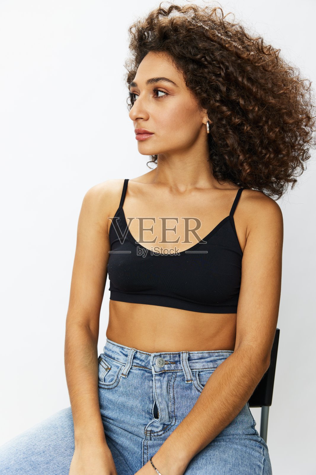 留着卷发的女模特在白色背景的椅子上摆姿势，自由地移动和跳舞，看着镜头，复制空间照片摄影图片