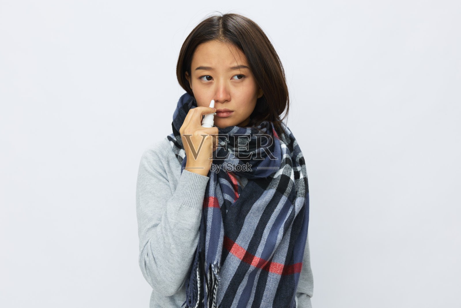 亚洲女性感冒鼻塞拿着鼻喷雾剂，用白色背景喷雾剂喷治过敏和喉咙痛的新冠病毒照片摄影图片