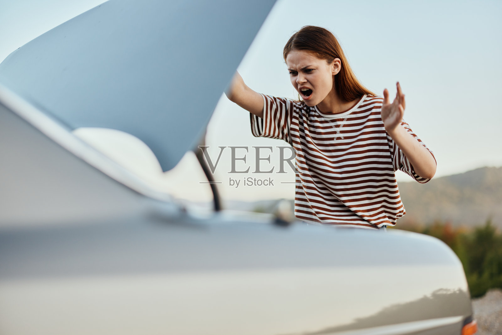 女人打开后备箱，愤怒地尖叫起来。汽车在自然道路上发生故障照片摄影图片