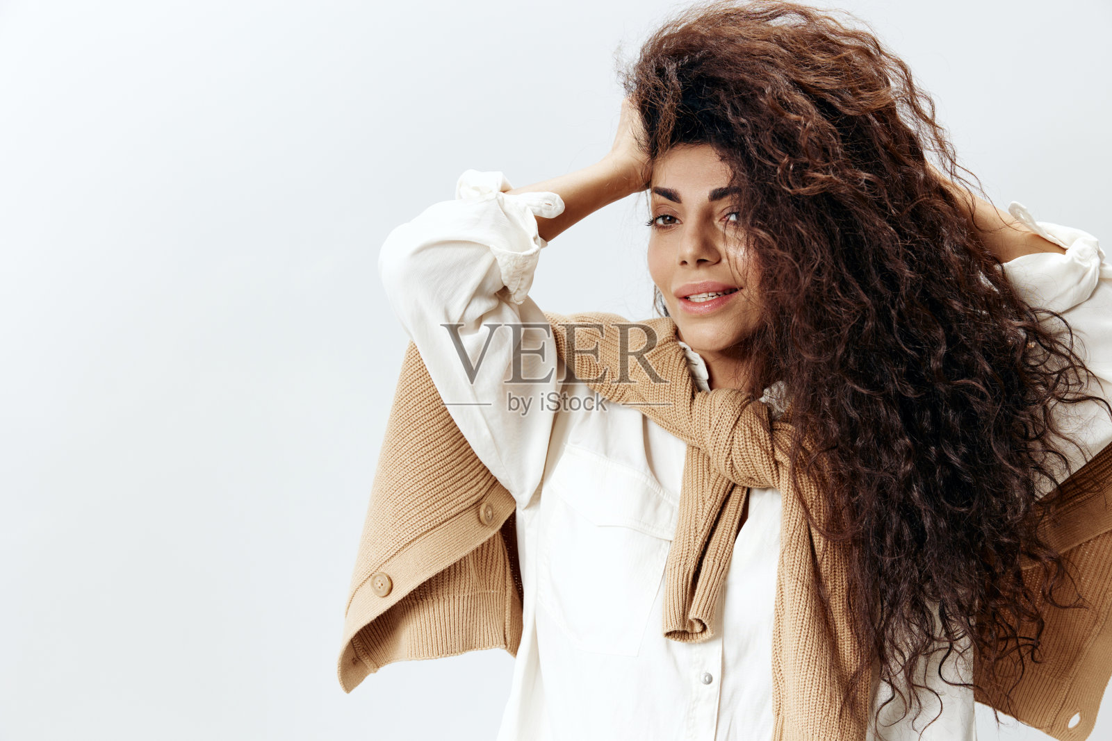 卷曲漂亮的拉丁女性肖像在柔和的温暖的毛衣和白衬衫触摸头发摆孤立的白色工作室墙背景。时尚季节性销售新系列概念。本空间照片摄影图片