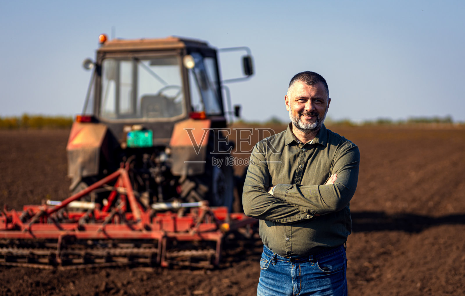 心满意足的成熟农民站在田间准备用拖拉机耕地的画像。照片摄影图片