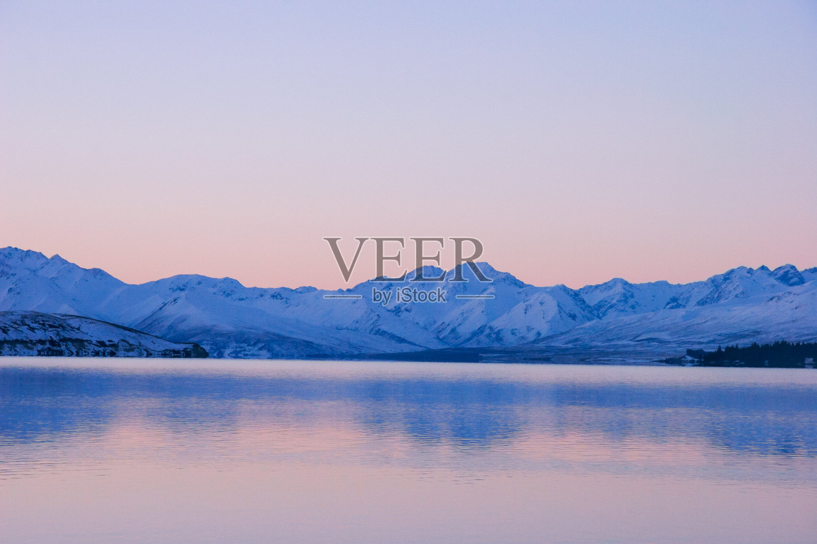 在新西兰南岛冰冷的蒂卡波湖上，令人难以置信的亮粉色和蓝色日落色调照片摄影图片