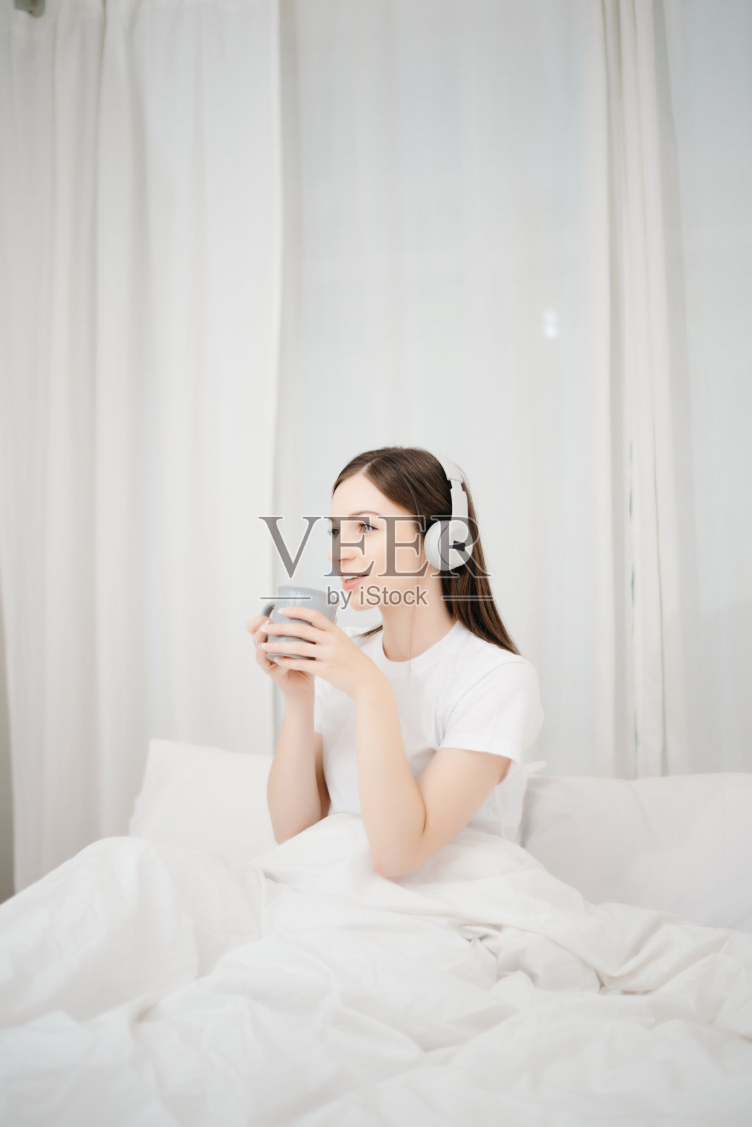 美丽的女人在白色的床上醒来，早上在家里端着咖啡照片摄影图片