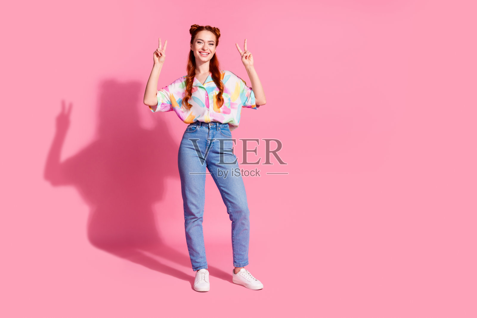 有趣的女孩的全身照片穿着印花衬衫牛仔裤裤子显示v字孤立在粉红色的背景照片摄影图片