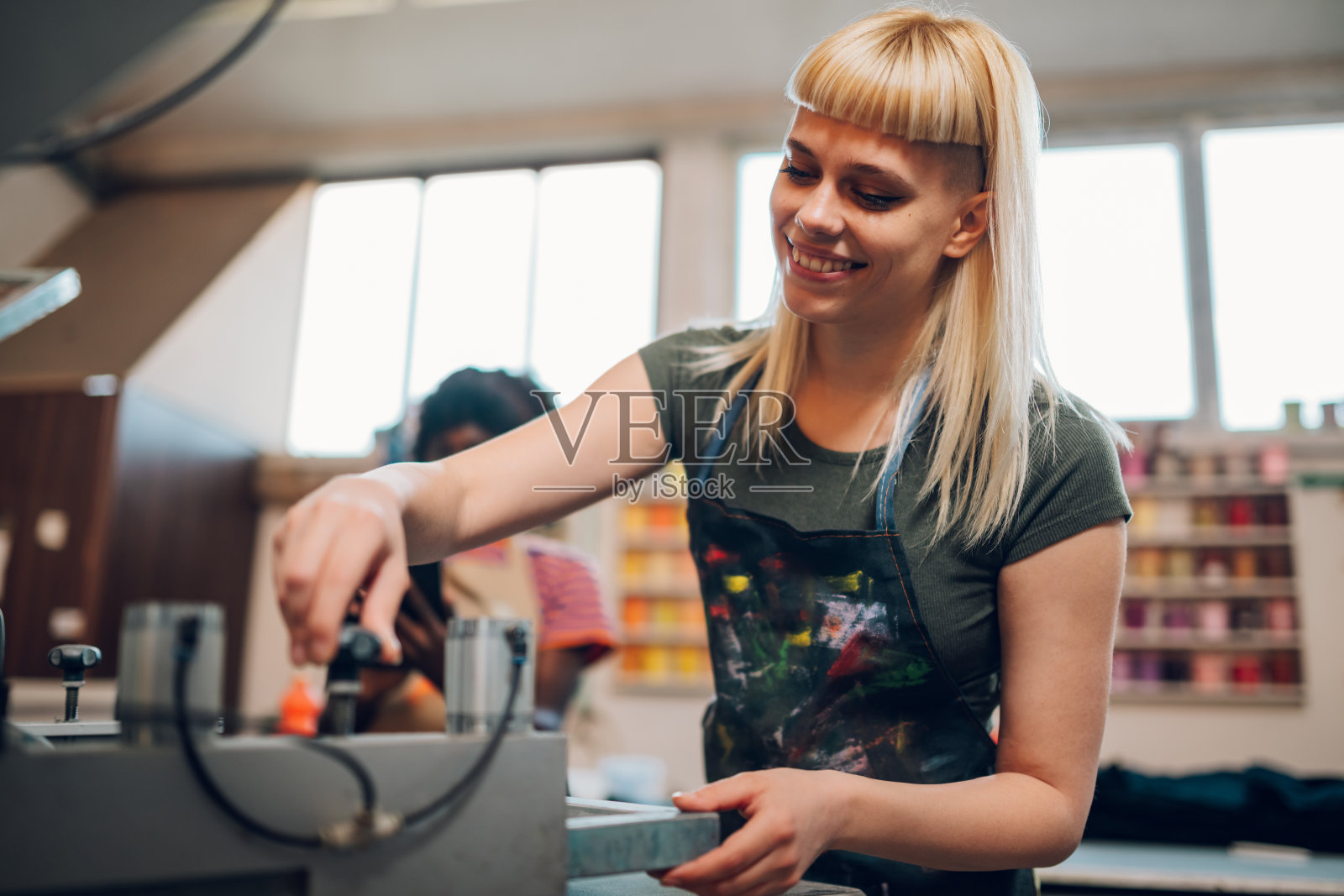 微笑的印刷工人在印刷车间操作丝网印刷机。照片摄影图片