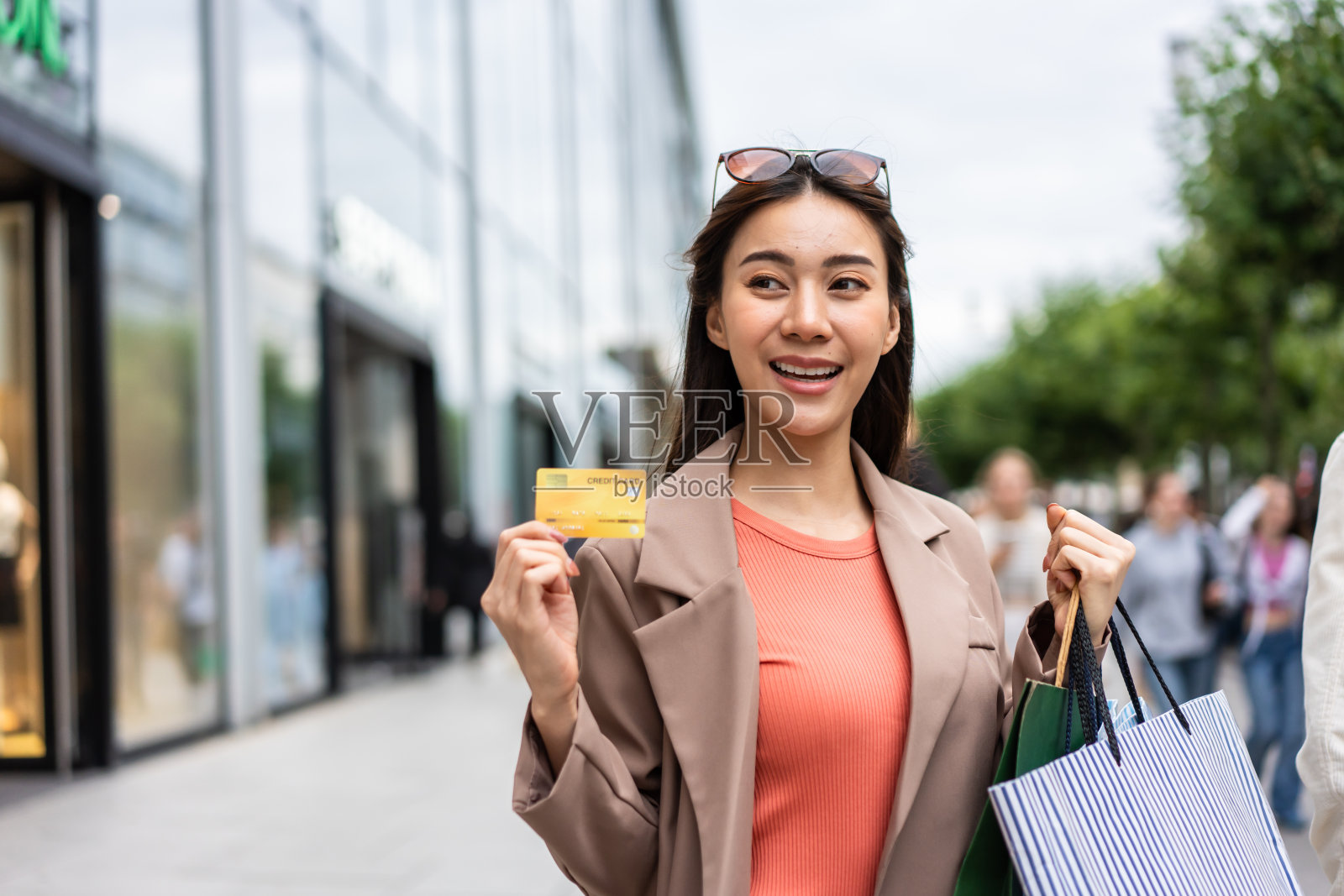 亚洲年轻美女在百货公司户外购物。有魅力的女性拿着购物袋和信用卡，然后快乐地独自走在购物中心的市场中心。照片摄影图片