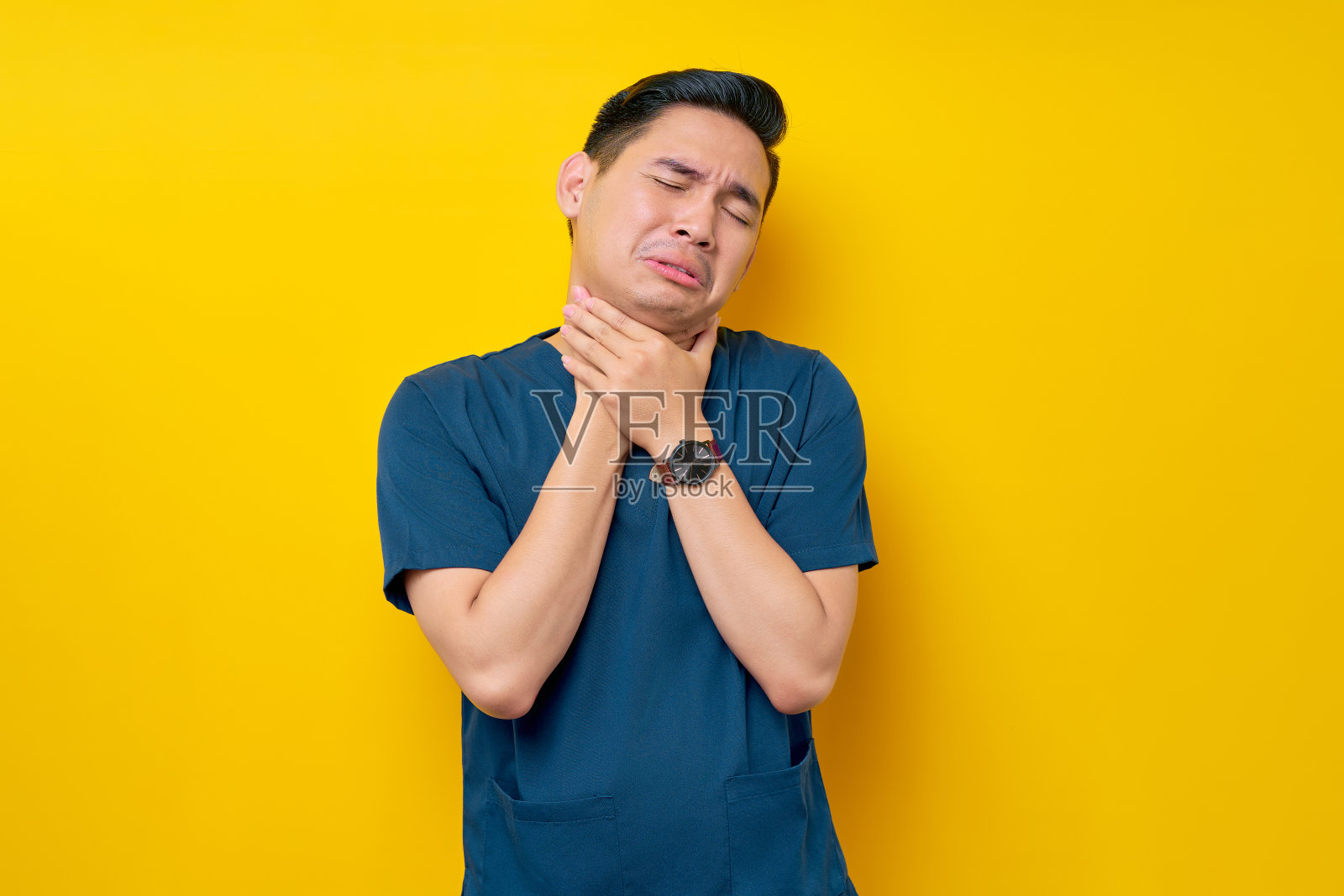 穿着蓝色制服的亚洲年轻专业男医生或护士在长时间孤立的黄色背景下久坐后感到不适，颈部疼痛照片摄影图片