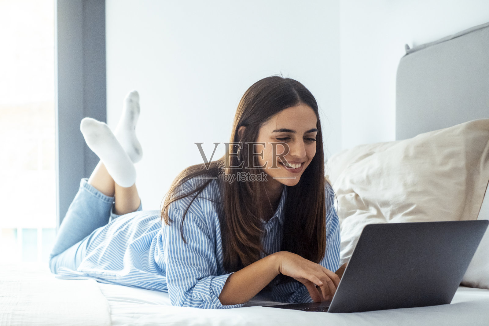 一位年轻的女士独自躺在卧室的床上放松地上网。旅游商务现代在线人在酒店客房工作。一名妇女放松地使用笔记本电脑照片摄影图片