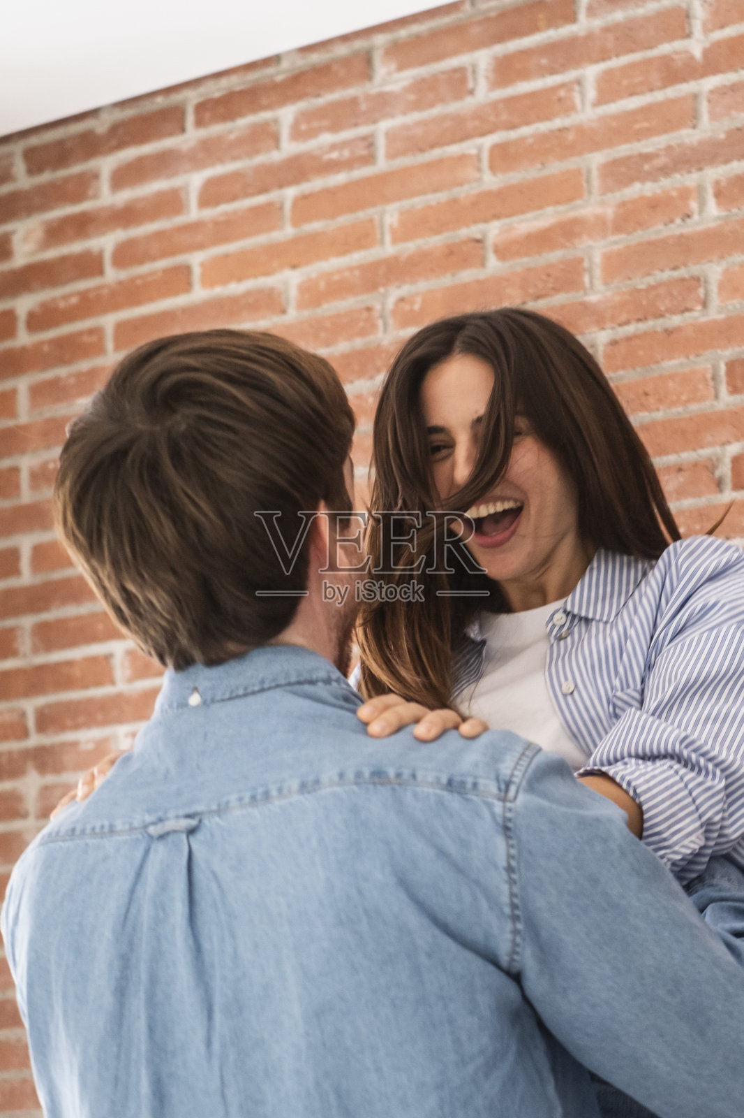 快乐的年轻夫妇在家里一起庆祝，玩得开心，笑得很开心。男人用爱和友谊拥抱女人。成就和成功的概念。关系和约会室内的人照片摄影图片