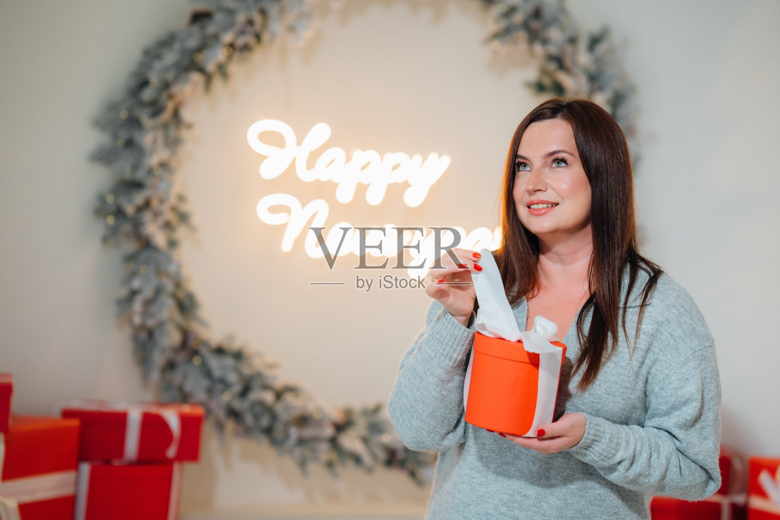 迷人的黑发女人拿着红色盒子里的圣诞礼物。照片摄影图片