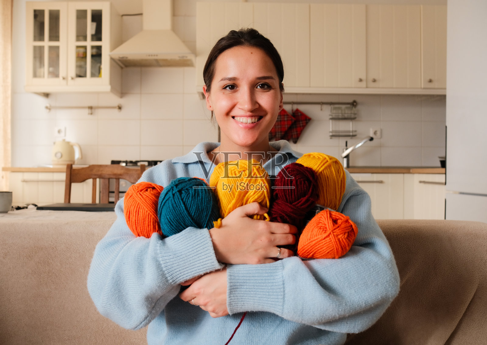 一个女孩坐在舒适的家里的沙发上，手里拿着许多五颜六色的纱线球照片摄影图片