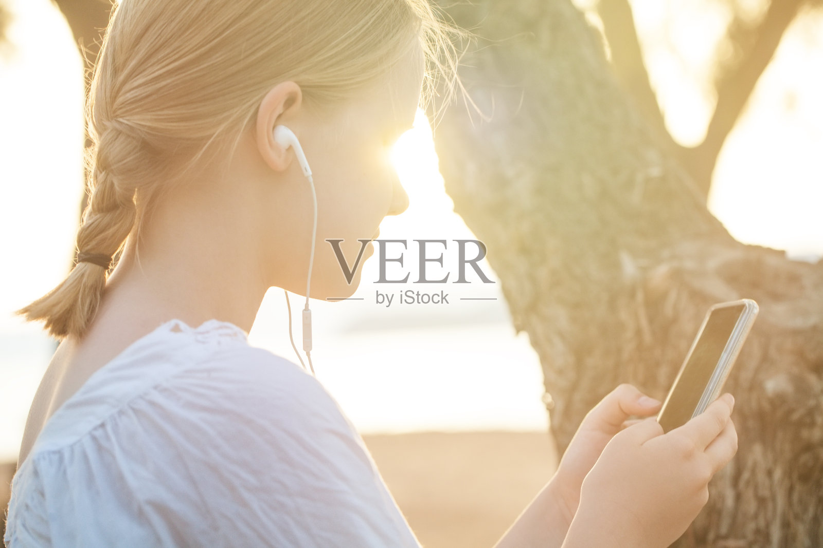 幸福微笑的金发少女肖像，戴着耳机，拿着手机，侧身站在大海的背景上照片摄影图片