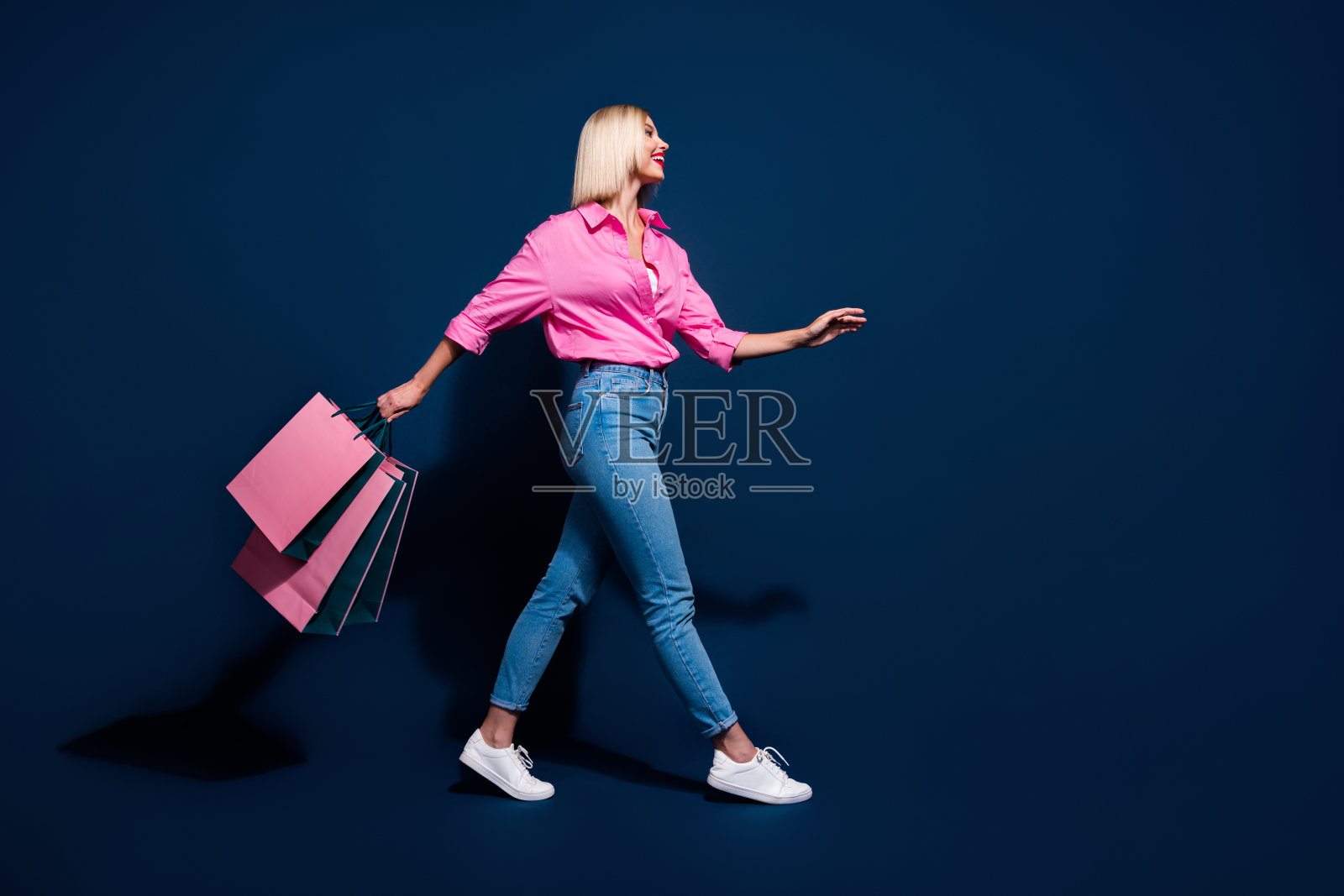 漂亮的年轻女孩的全尺寸照片走享受购物持有包穿时髦的粉红色服装孤立的深蓝色背景照片摄影图片