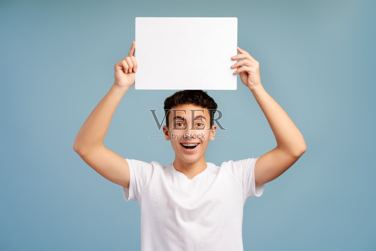 兴奋，微笑的男孩带着牙套拿着白色的空白屏幕看着镜头照片摄影图片