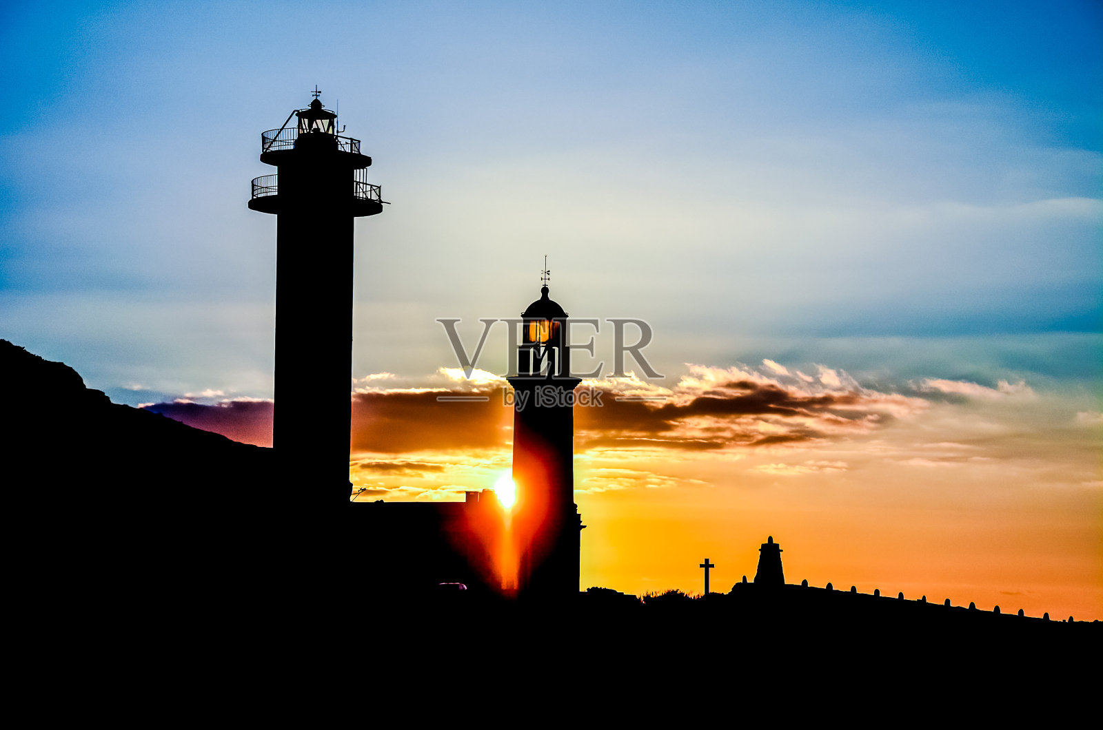 美丽的夕阳映衬出一座灯塔和一座小楼的剪影照片摄影图片