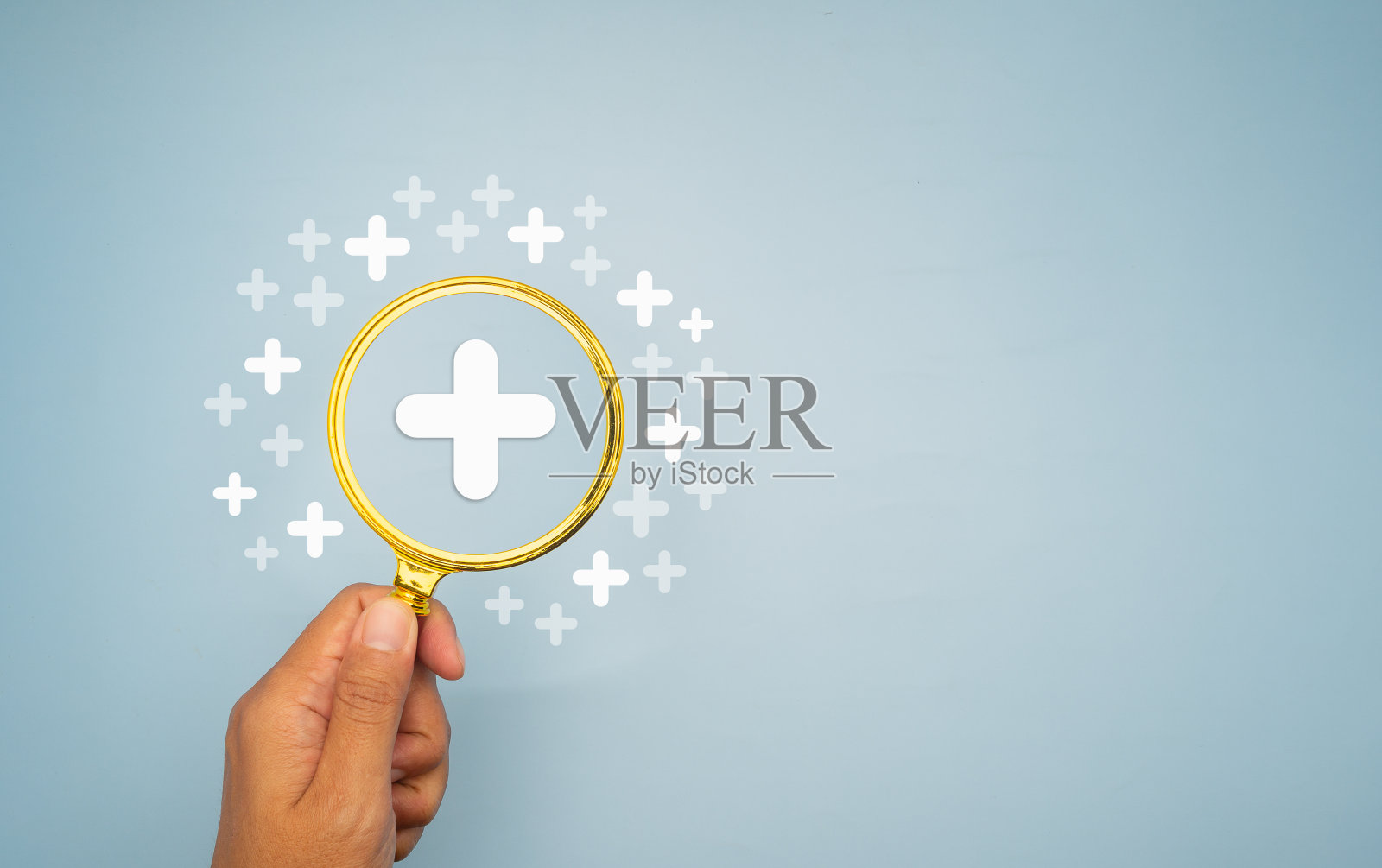 手拿着放大镜，背景是浅蓝色的白色加号。照片摄影图片