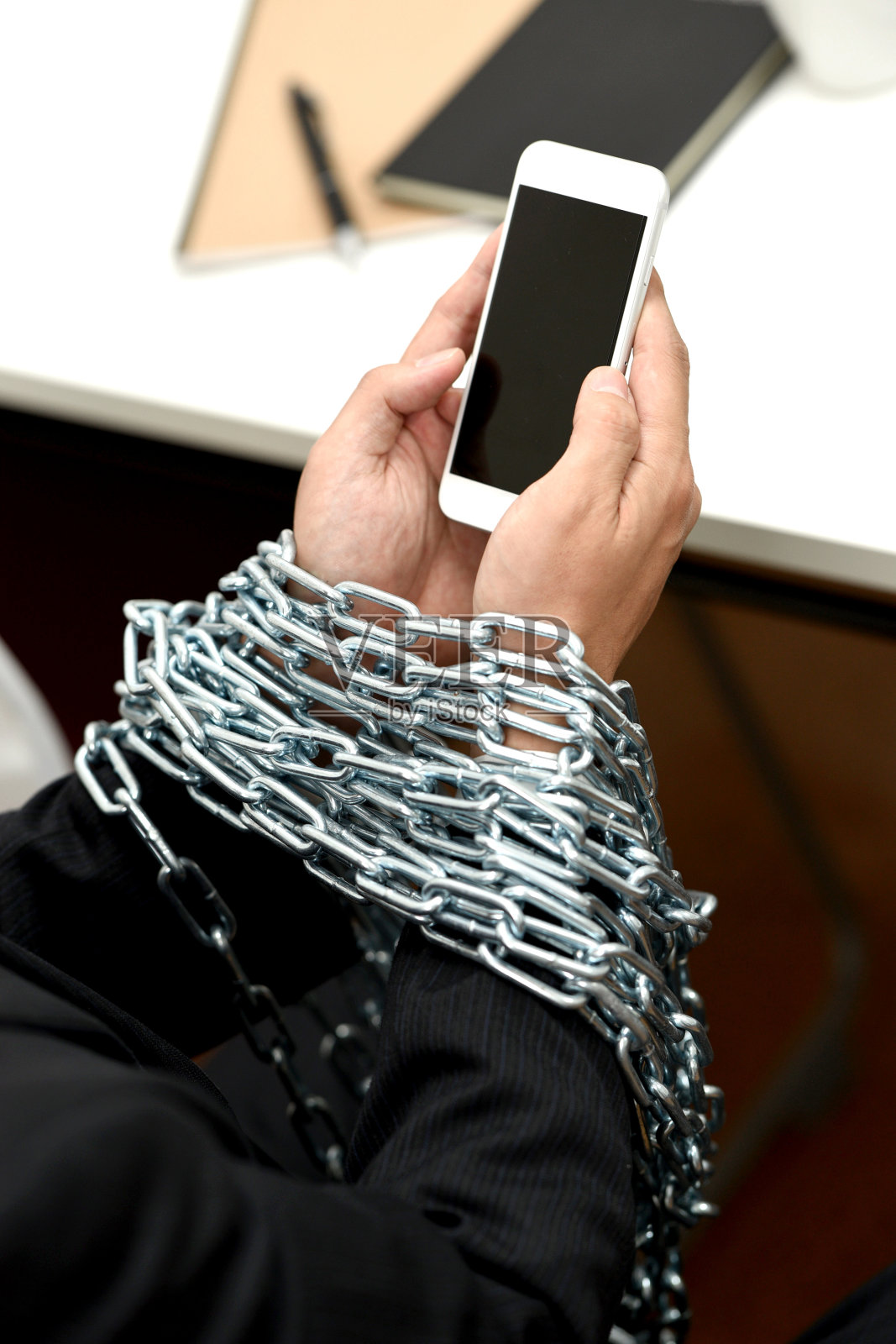 戴着链子、在笔记本电脑前操作智能手机的上班族的手照片摄影图片