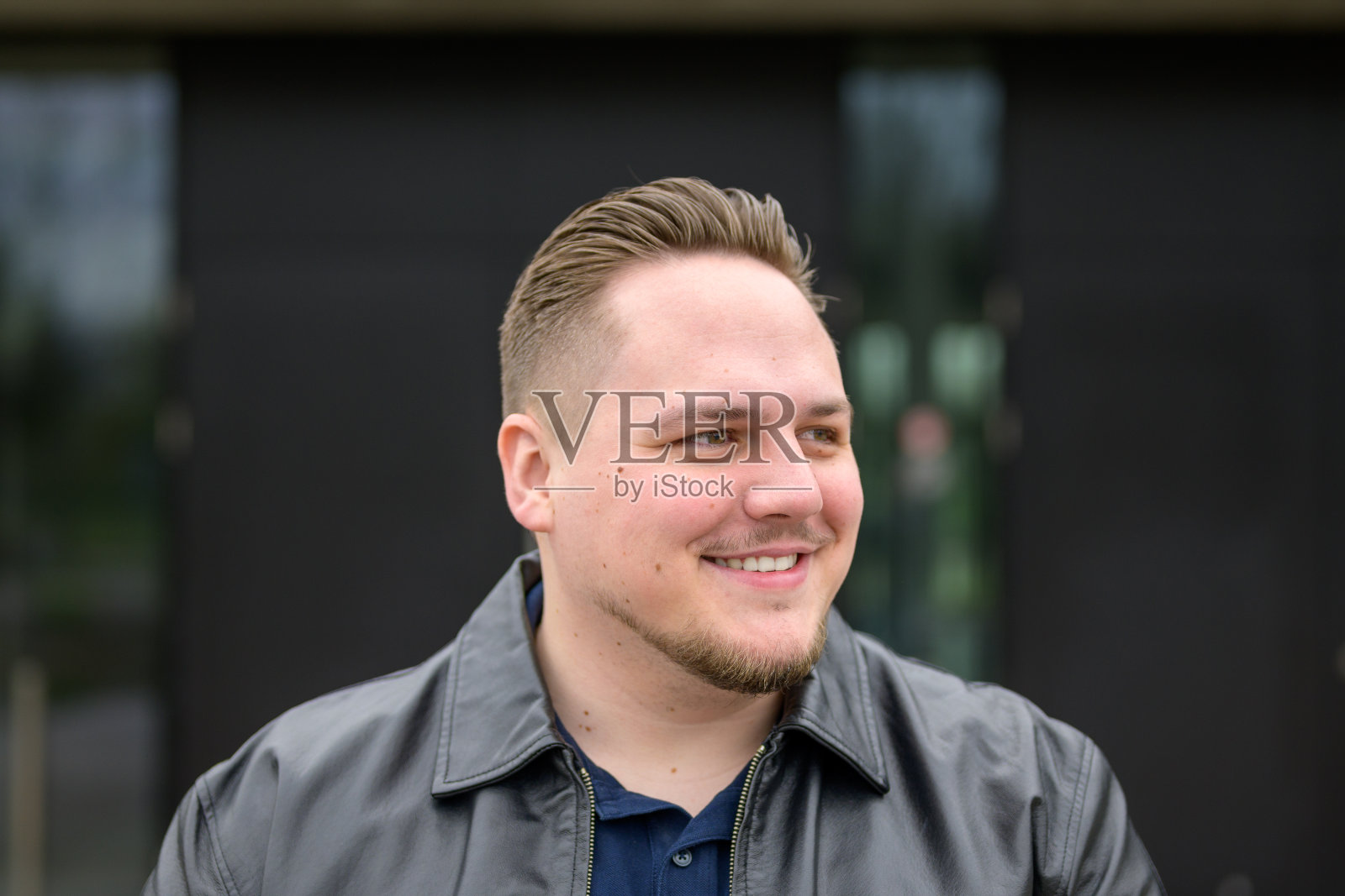 一个穿着黑色皮夹克，梳着光滑的背头的年轻人，在旁边看起来很友好照片摄影图片